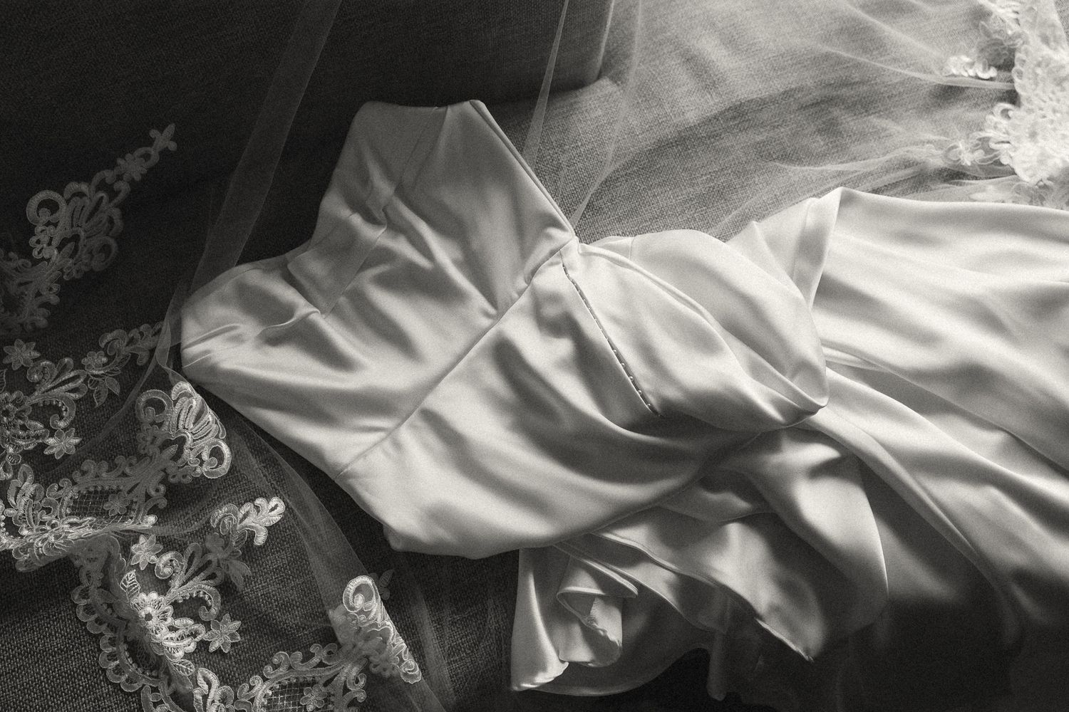 Black and white close-up of a strapless satin wedding gown with lace veil draped alongside.