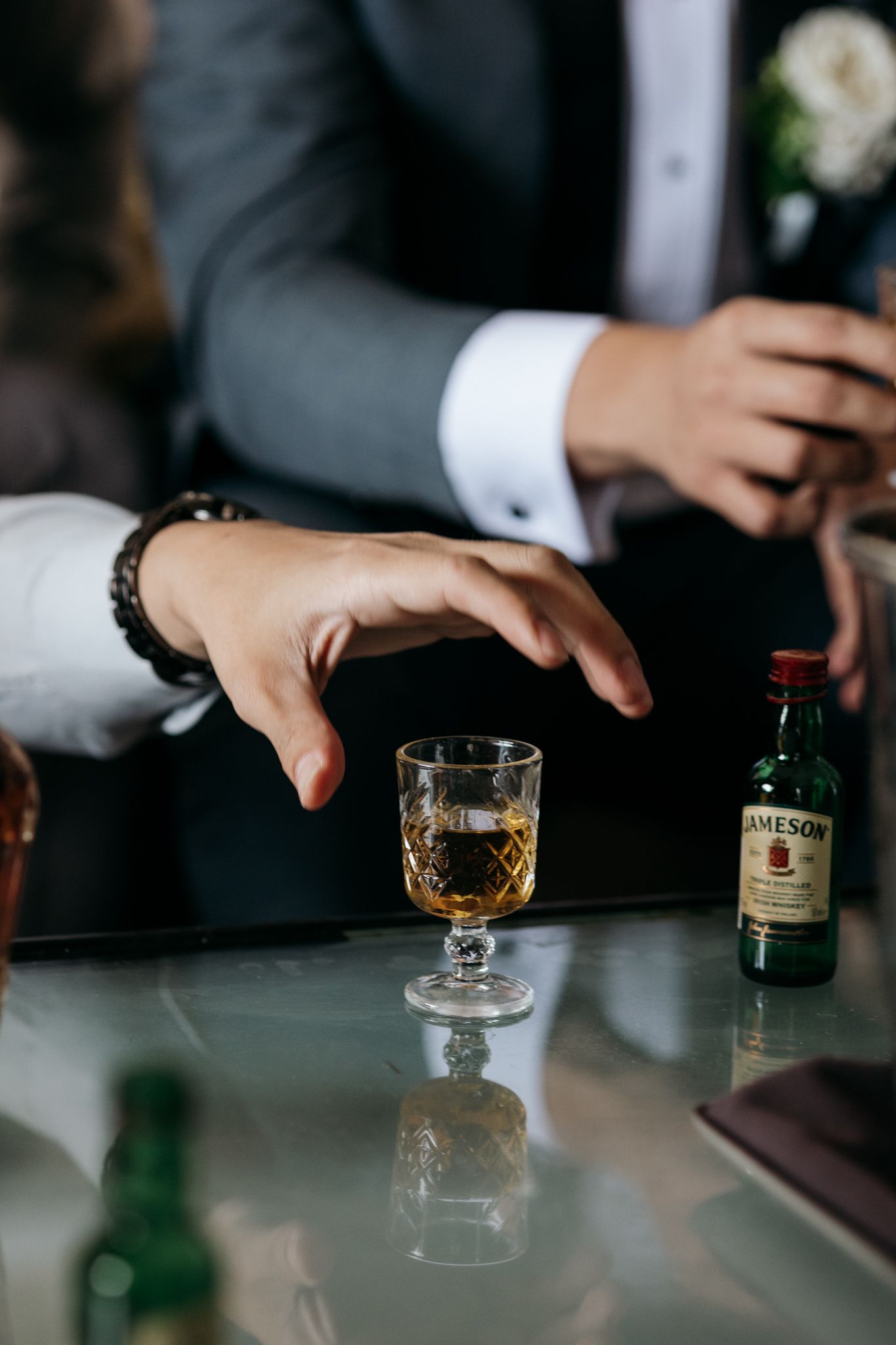 Hand reaching for a crystal shot glass of Jameson Irish whiskey on a glass table at a formal event.