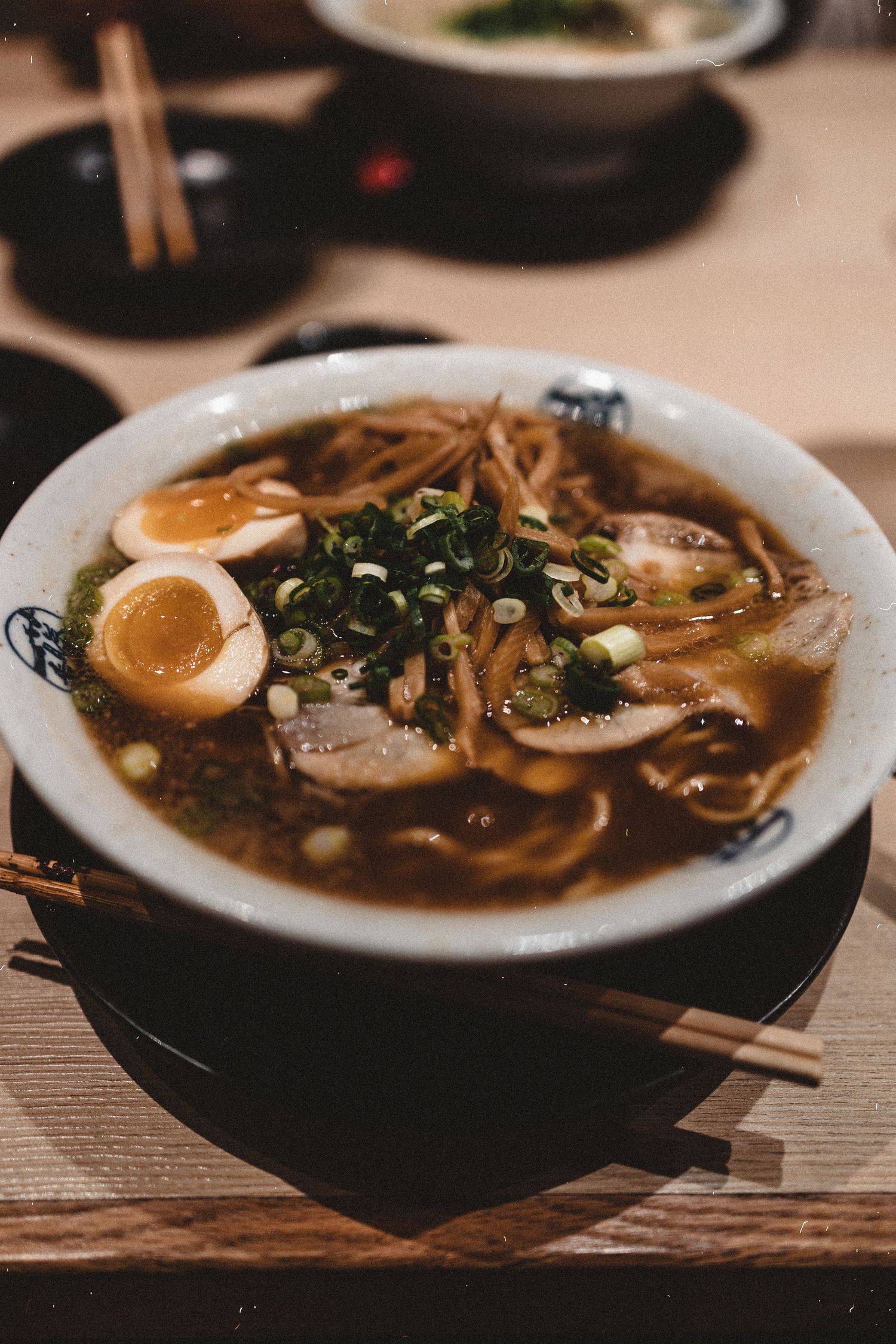 A bowl of rich Japanese ramen with soft-boiled egg, chashu pork, green onions, and noodles in dark broth.