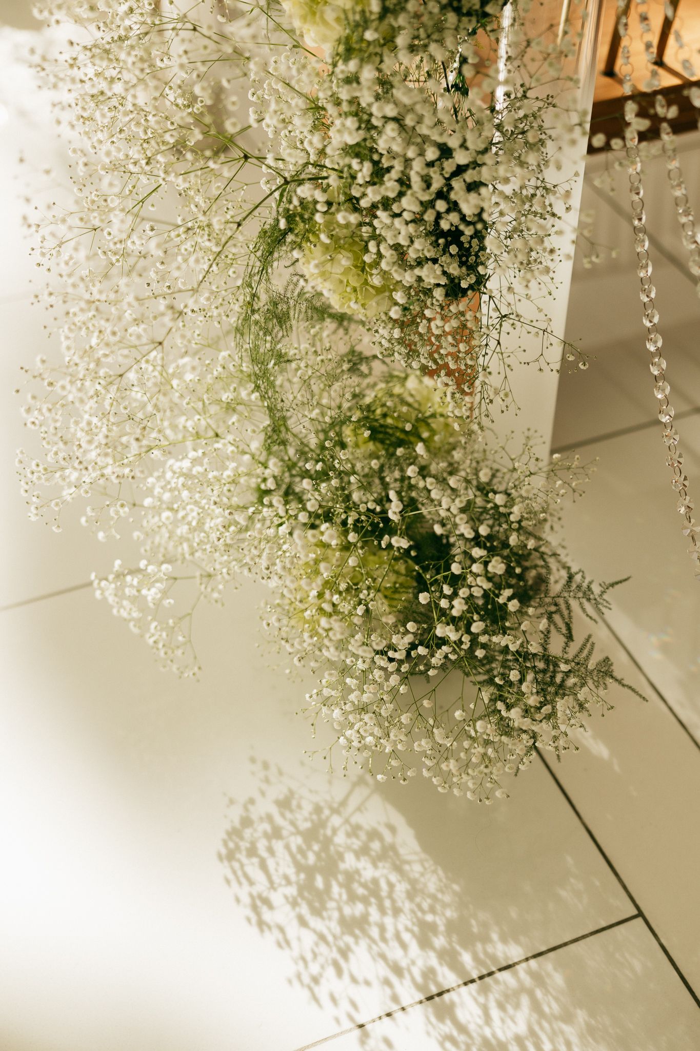 Elegant baby's breath floral arrangement cascading down a white pillar with crystal accents at a wedding venue.