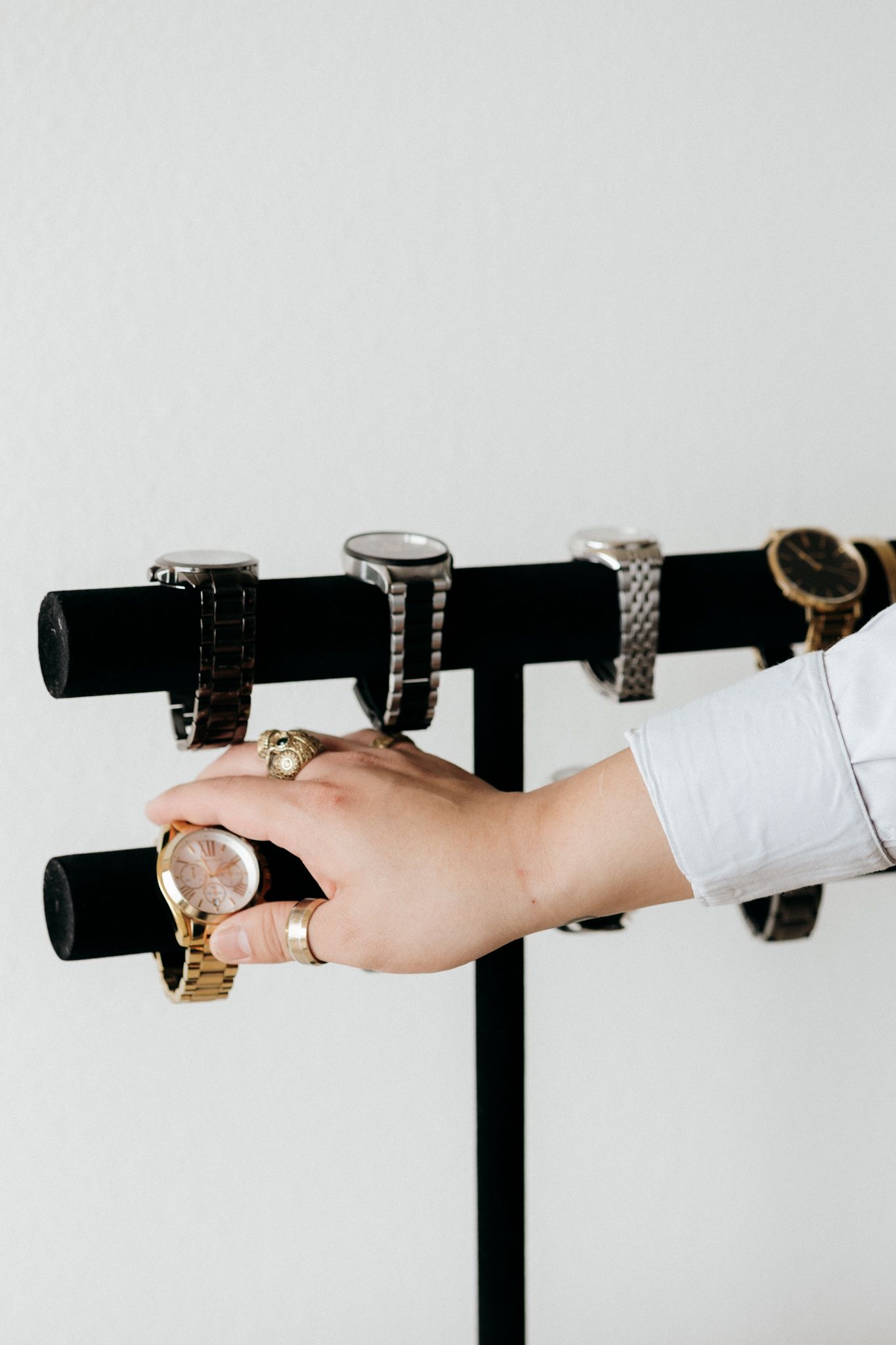 Hand selecting a gold watch from a black T-bar watch stand displaying multiple watches.