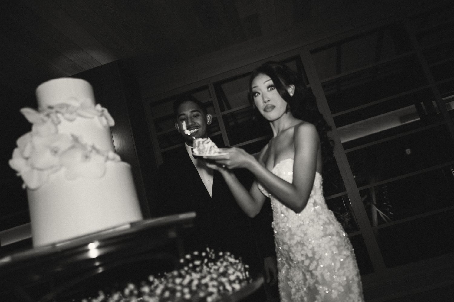 Black and white photo of a couple cutting their wedding cake at their elegant reception celebration.