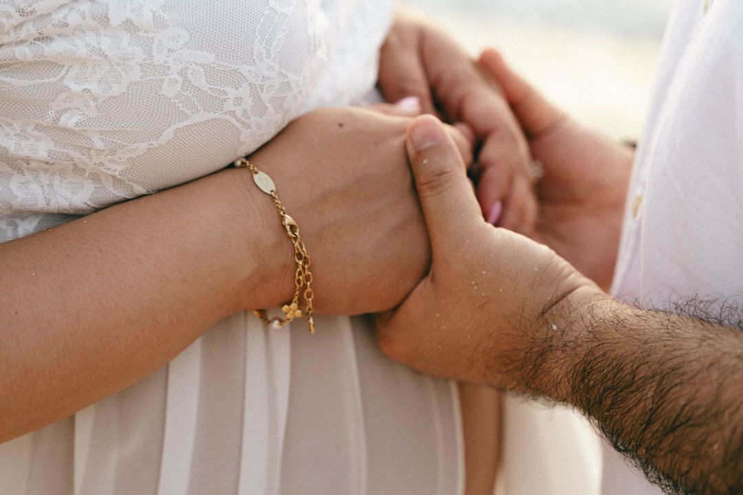 Close-up of a couple holding hands, woman wearing a gold chain bracelet, in a romantic outdoor setting.