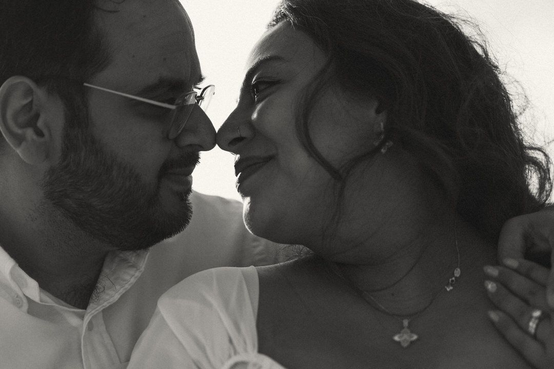 Black and white romantic couple portrait, man with glasses and beard leaning close to smiling woman outdoors.