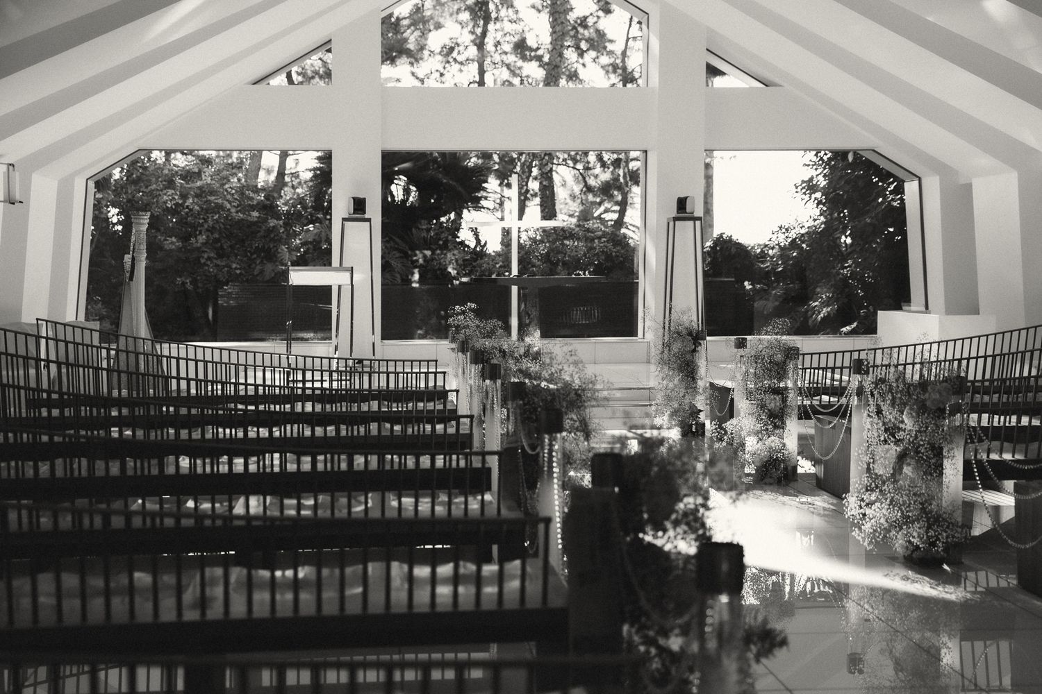 Black and white photo of an elegant chapel interior with rows of pews and large windows overlooking lush greenery.