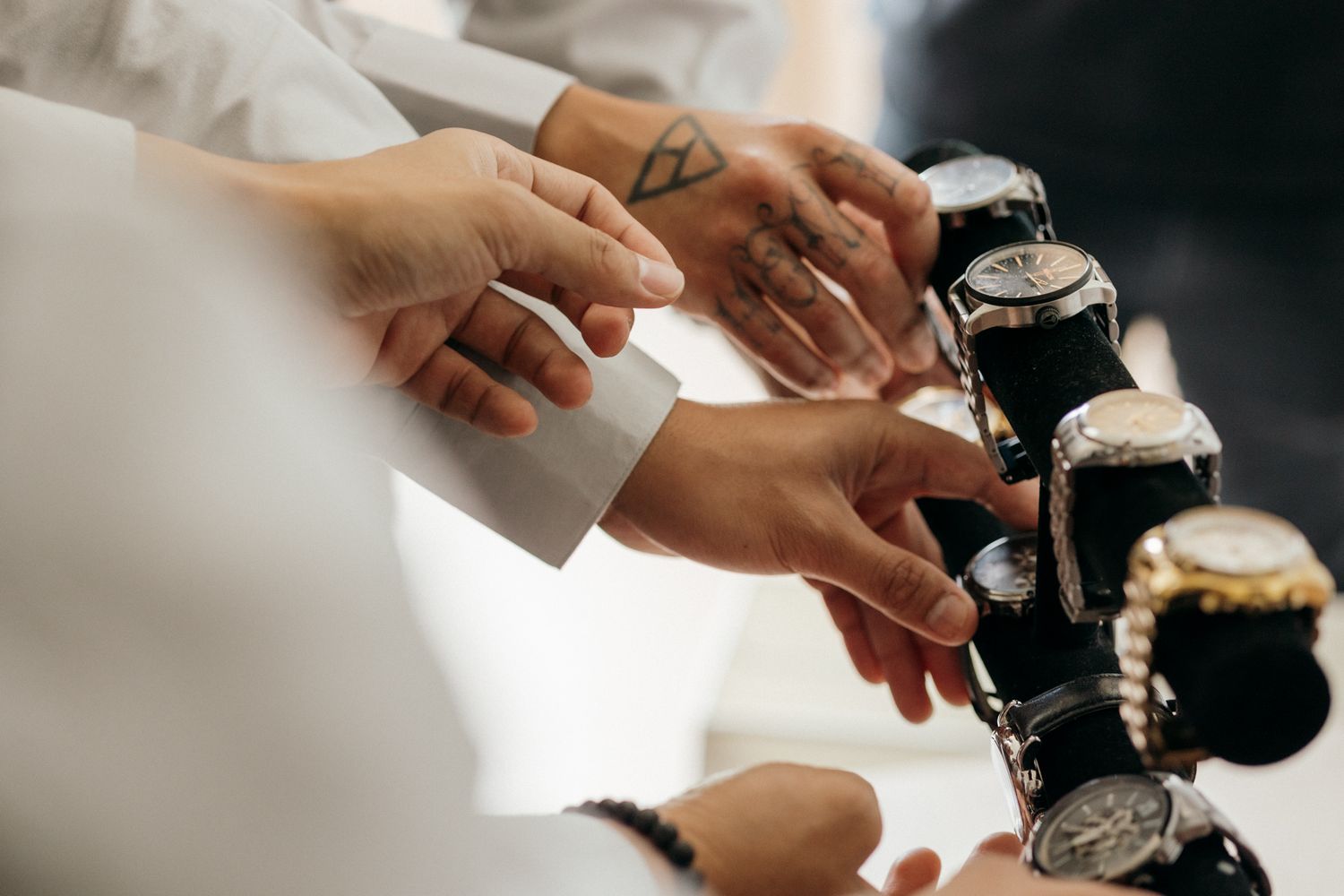 Multiple hands reaching for luxury wristwatches displayed on a stand in an upscale watch boutique.