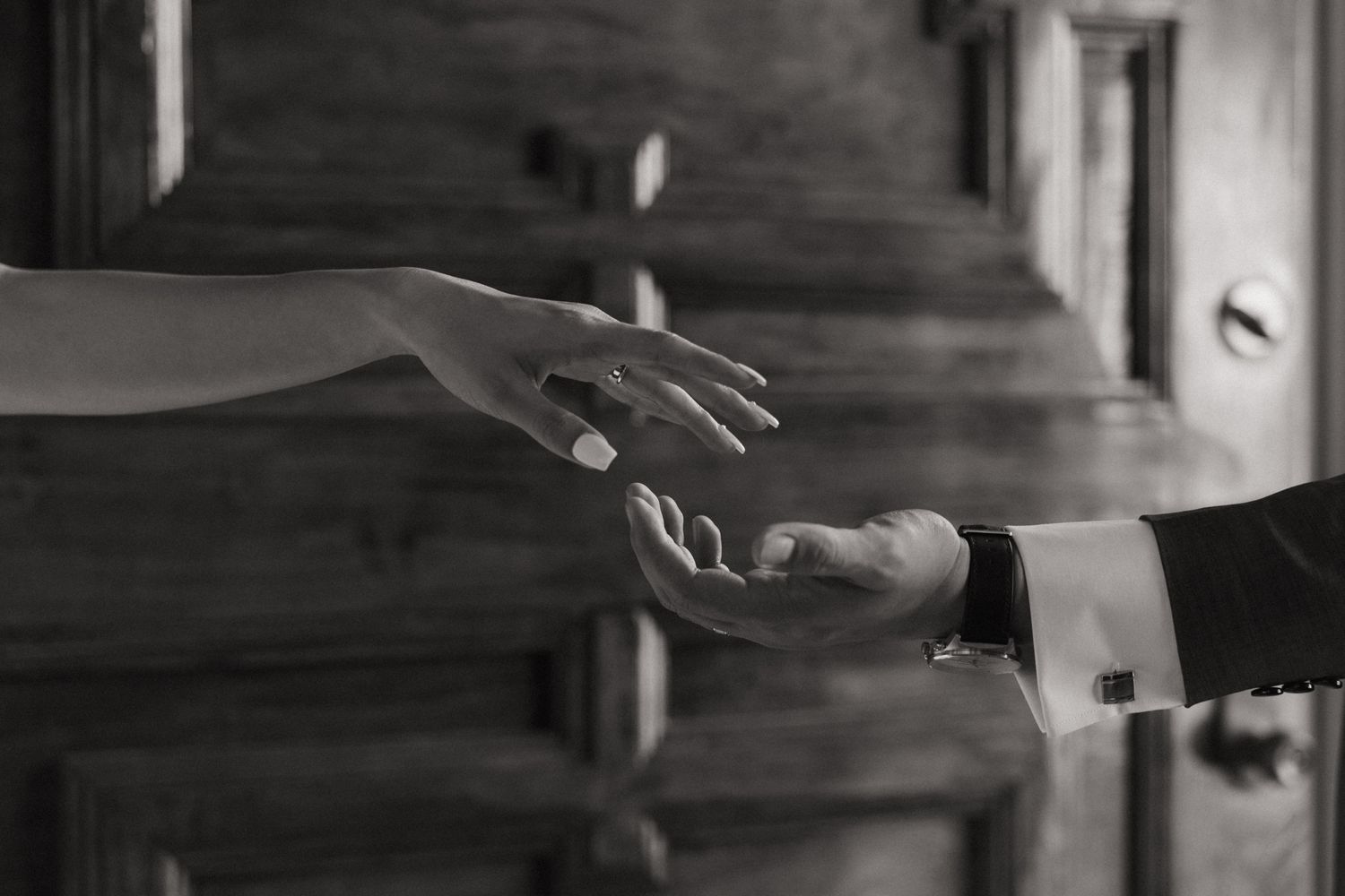 Black and white photo of two hands almost touching, bride and groom reaching for each other near wooden stairs.