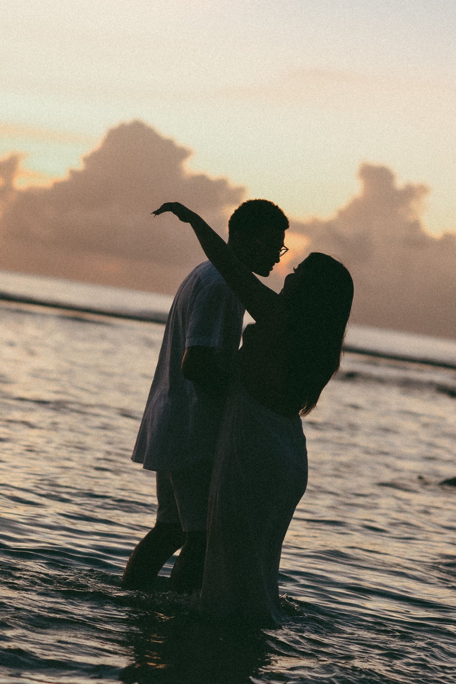Romantic couple silhouetted against a stunning ocean sunset, standing in shallow water during golden hour.