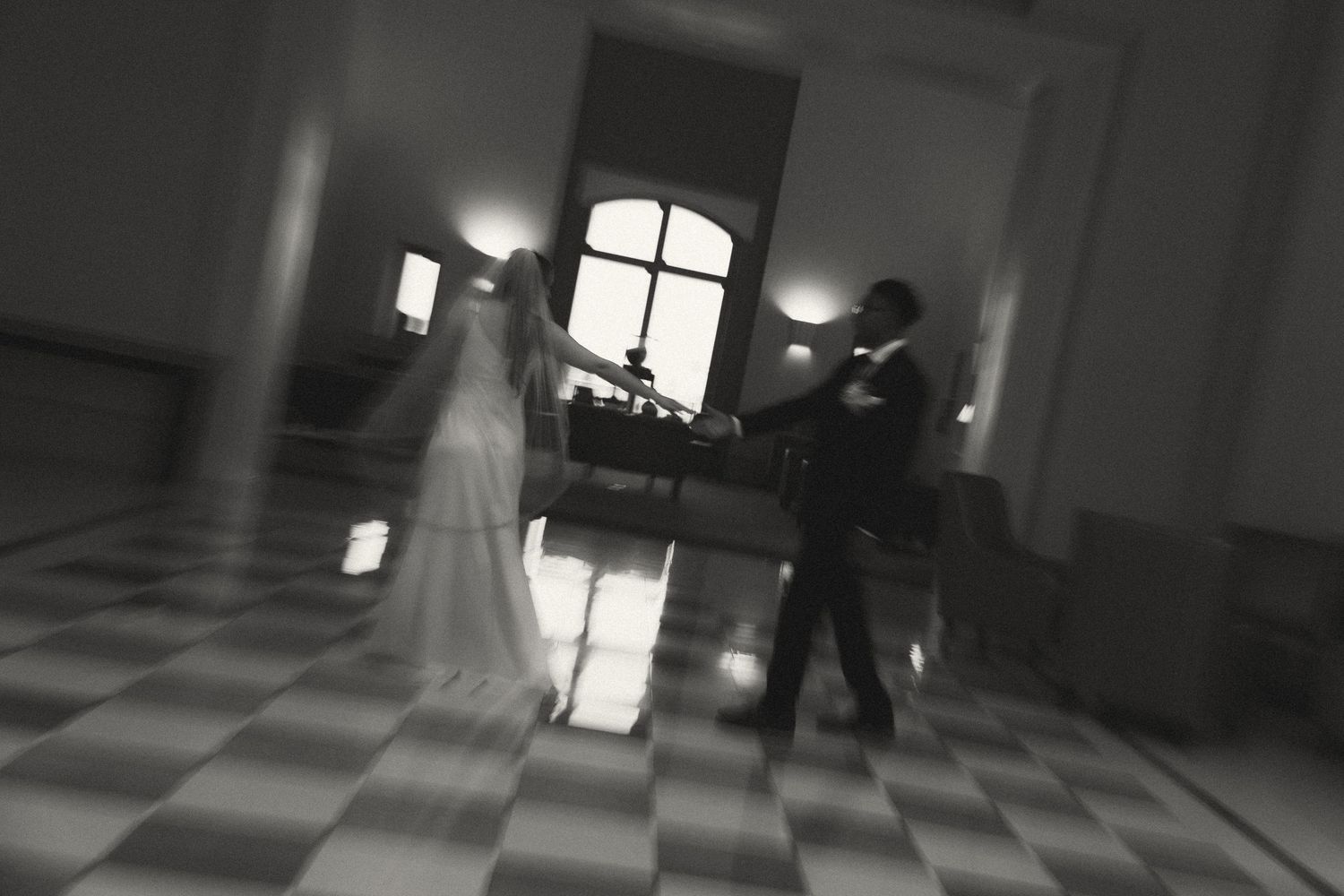 Black and white photo of a bride and groom sharing their first dance in an elegant ballroom.