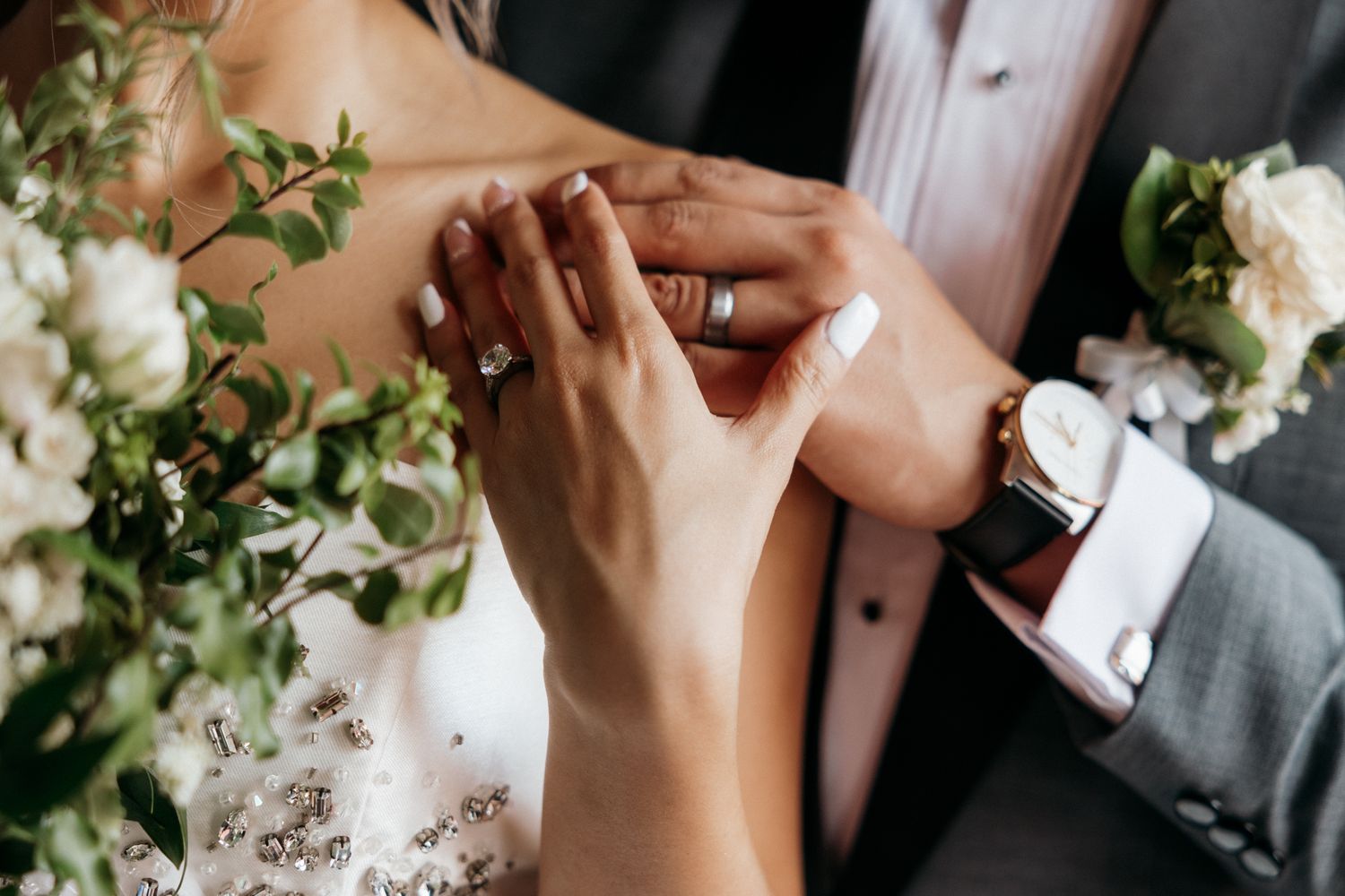 Close-up of bride and groom holding hands, showcasing diamond engagement ring and wedding bands on their wedding day.