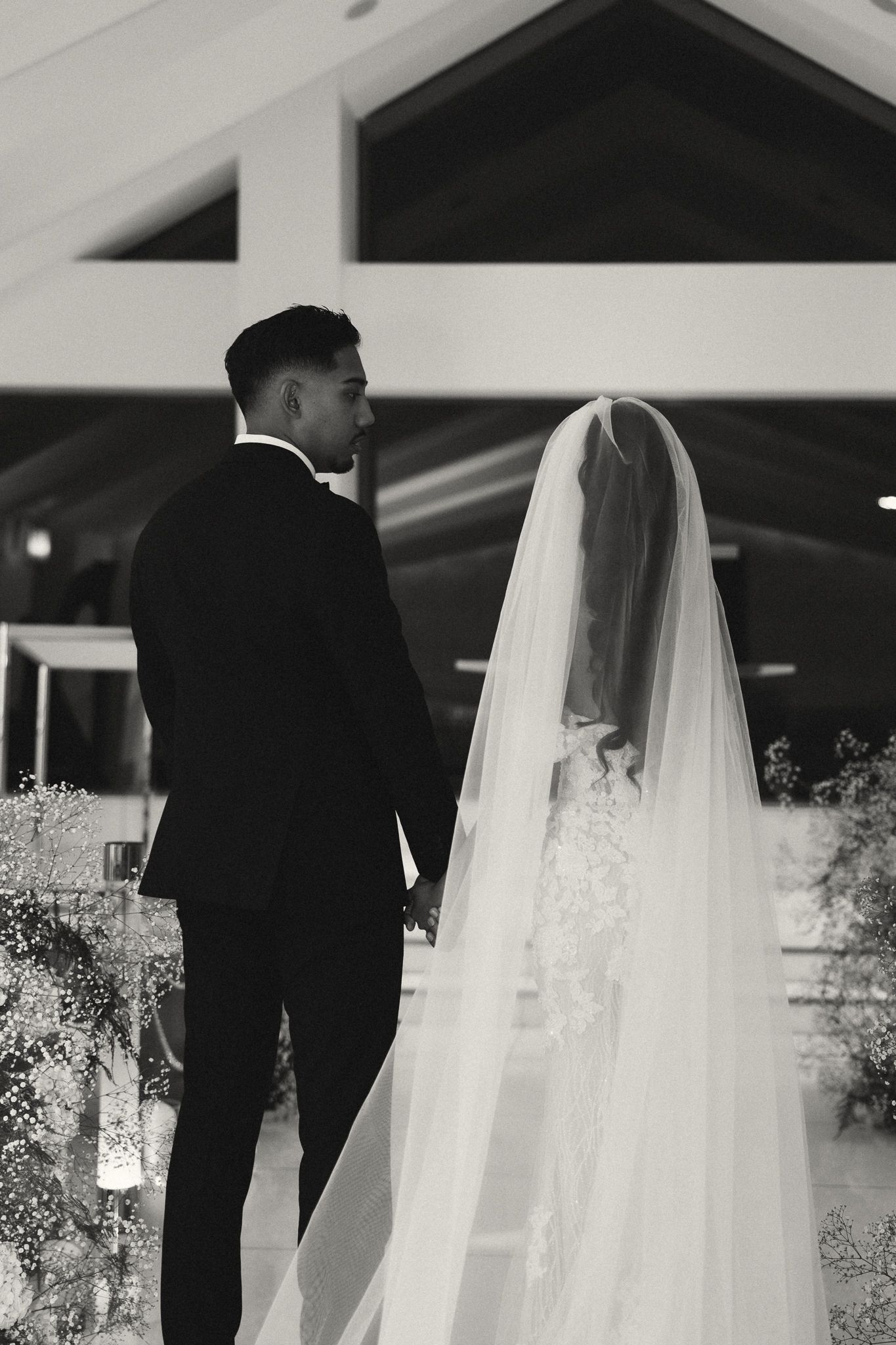 Black and white photo of a bride and groom holding hands at the altar during their wedding ceremony.