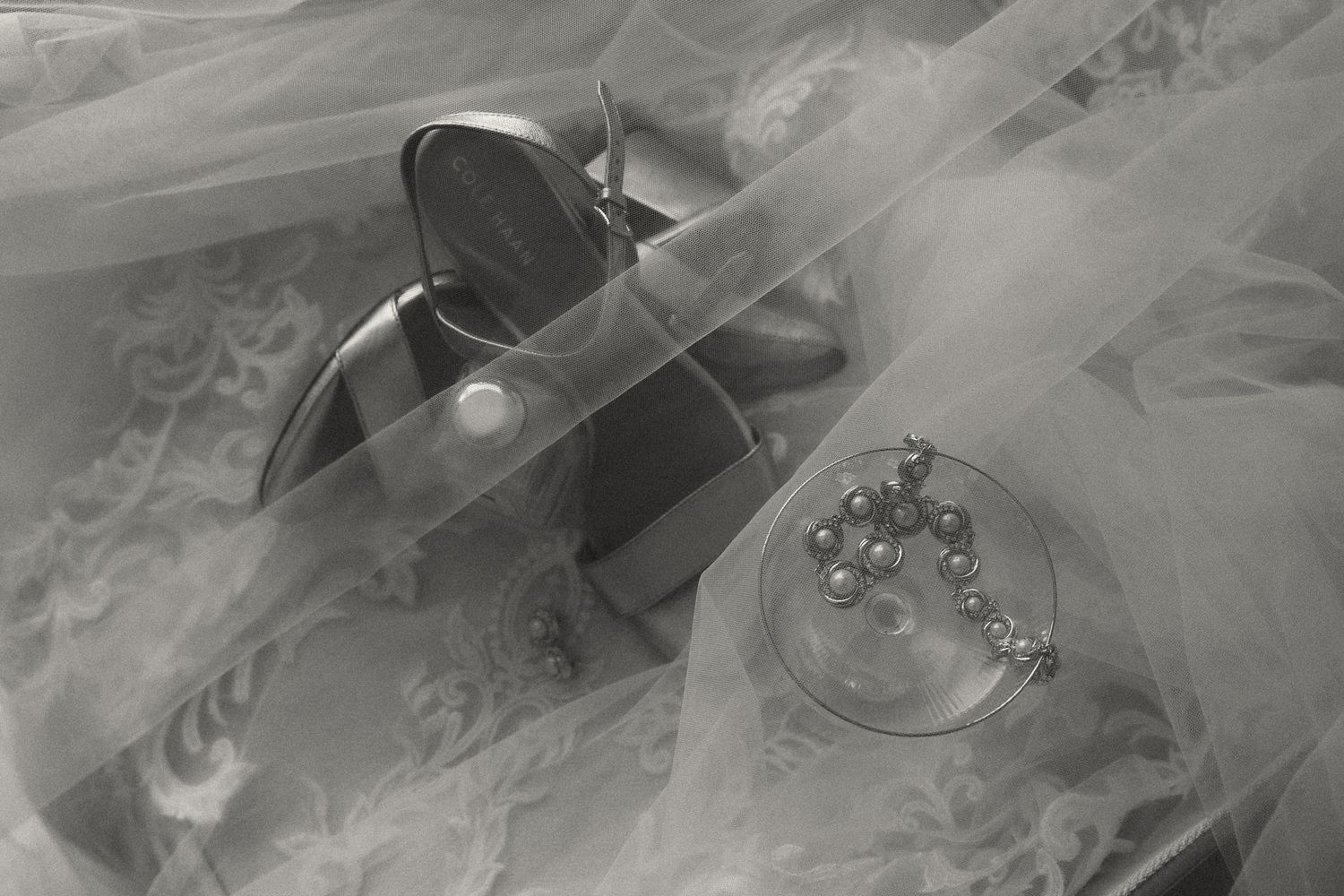 Black and white photo of a purse and pearl bracelet in a glass dish draped with sheer tulle fabric.