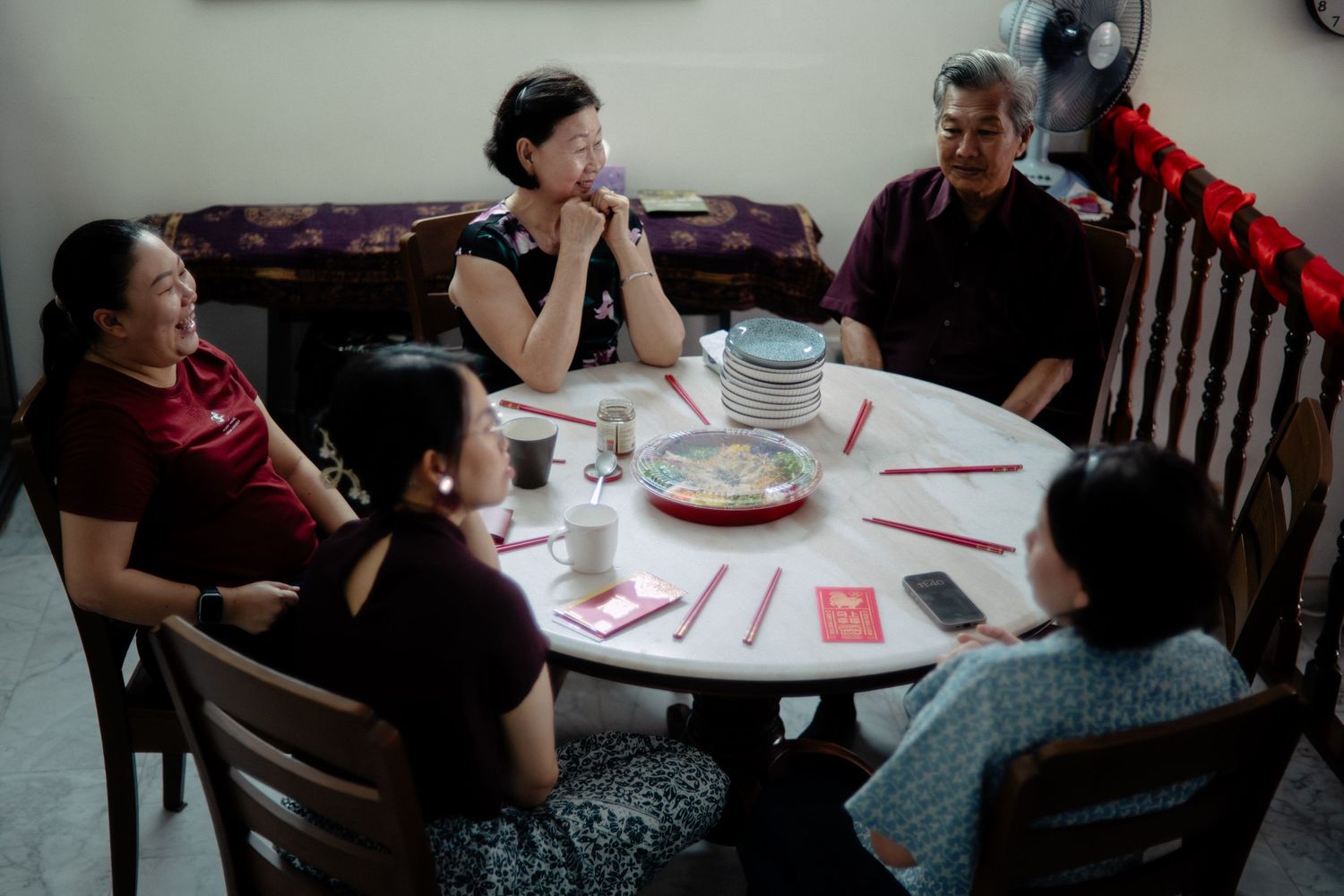 A group of five people sit around a round dining table sharing a meal and laughing together.