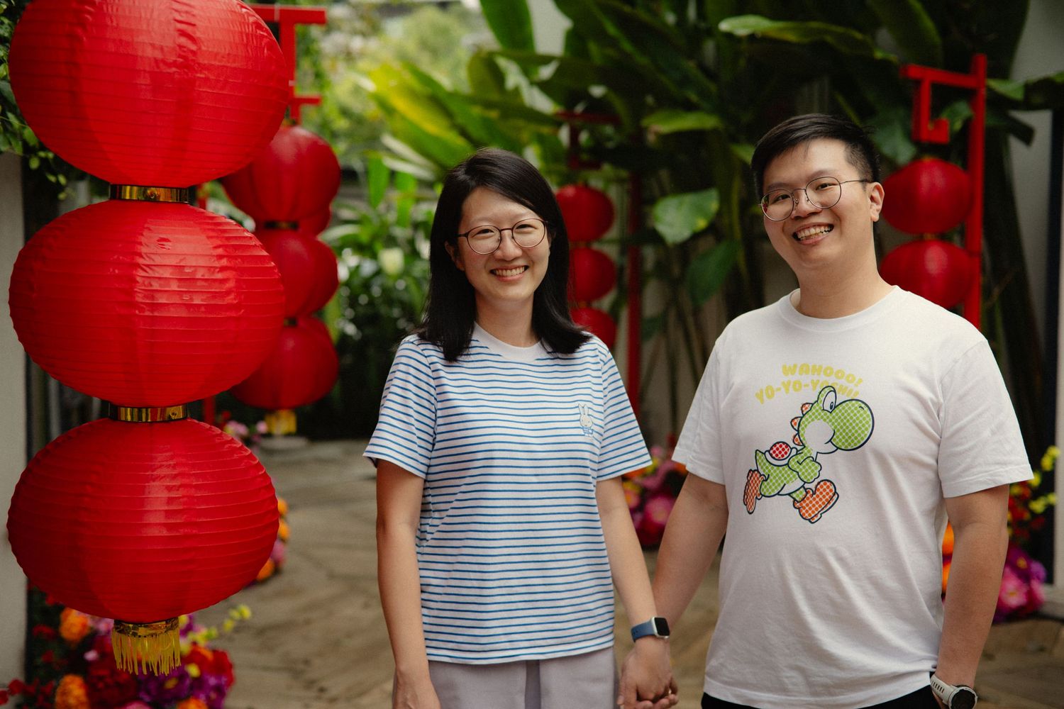 Smiling Asian couple holding hands beside vibrant red Chinese New Year lanterns.