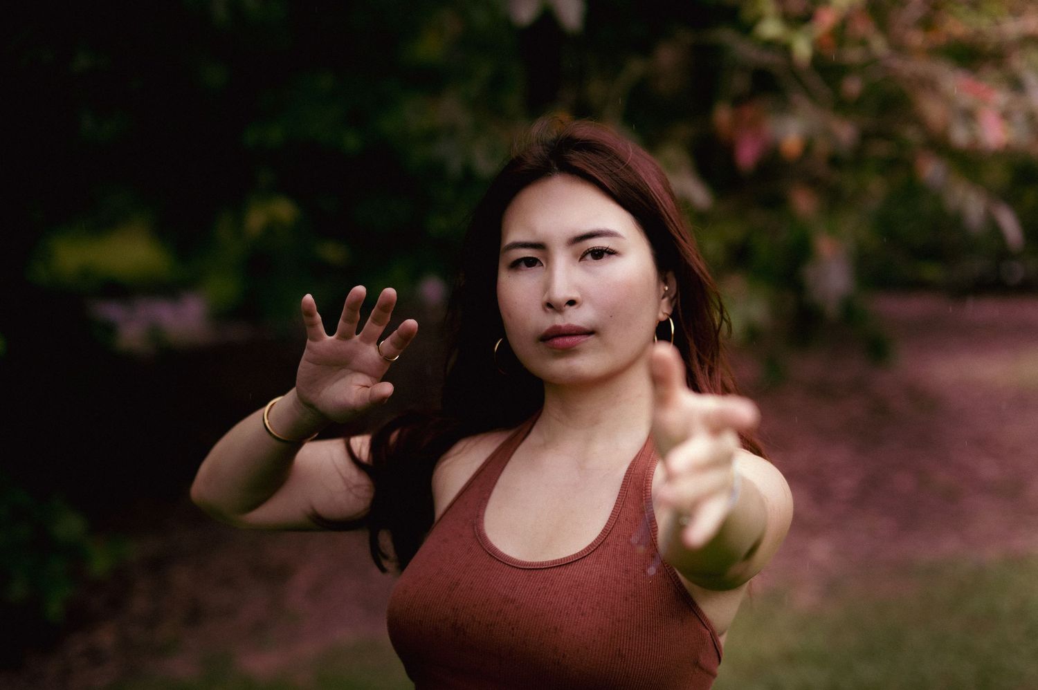 Young Asian woman reaching toward camera with both hands in an outdoor garden.