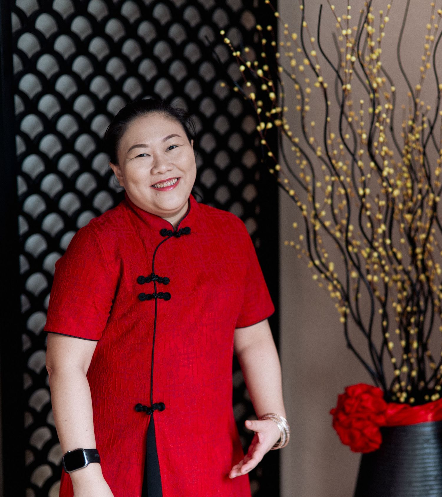 Smiling woman in a red traditional Chinese qipao dress posing indoors festively.