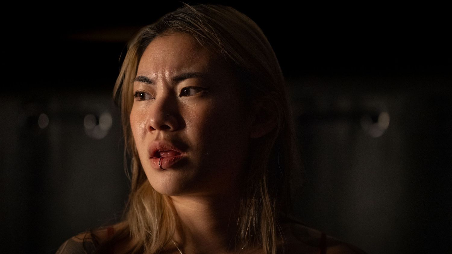 Close-up portrait of a young Asian woman with an intense expression in dramatic lighting.