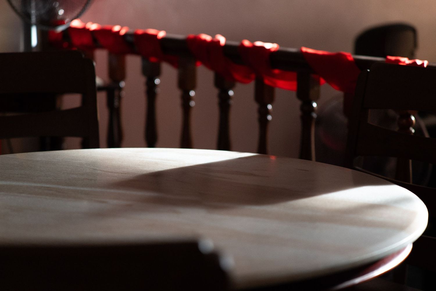 Close-up of round wooden table with dark chairs decorated with red flowers in dim light.