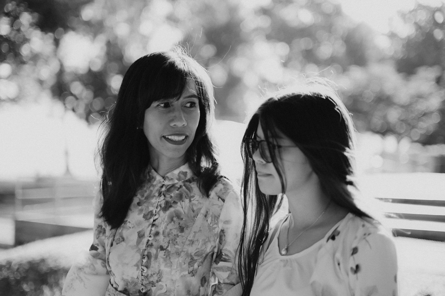 Black and white portrait of two dark-haired women sitting together outdoors on a bench.