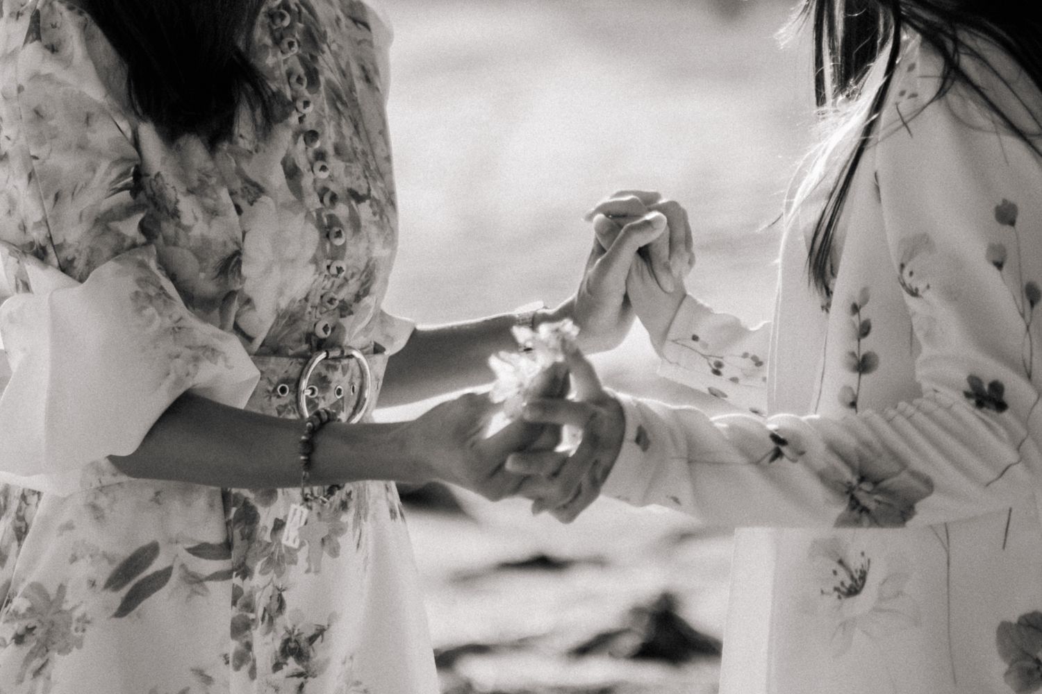 Two women in floral dresses holding hands in black and white outdoor photo.