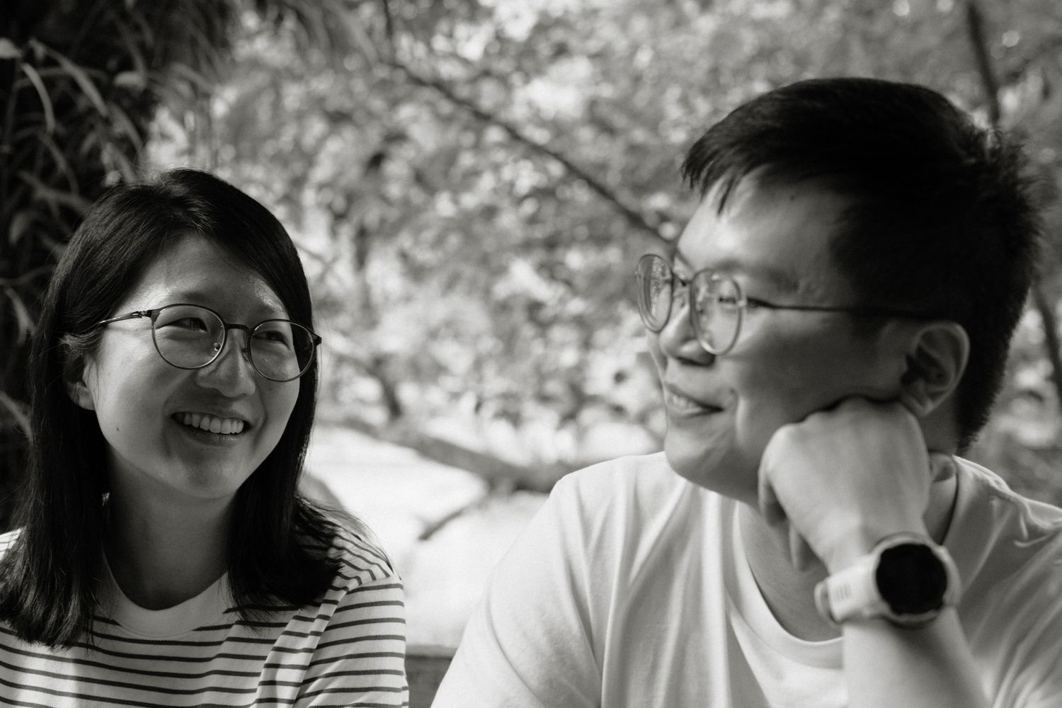 Black and white photo of a smiling young Asian couple laughing together outdoors.