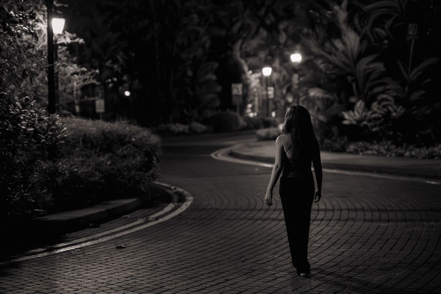 Black and white photo of a woman walking alone on a cobblestone path at night.