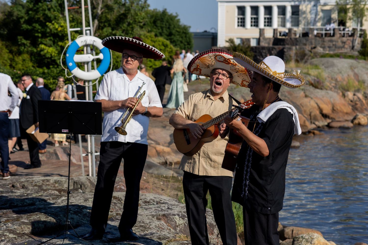 Mariachi band performing outdoors near waterfront rocks at a summer celebration event.
