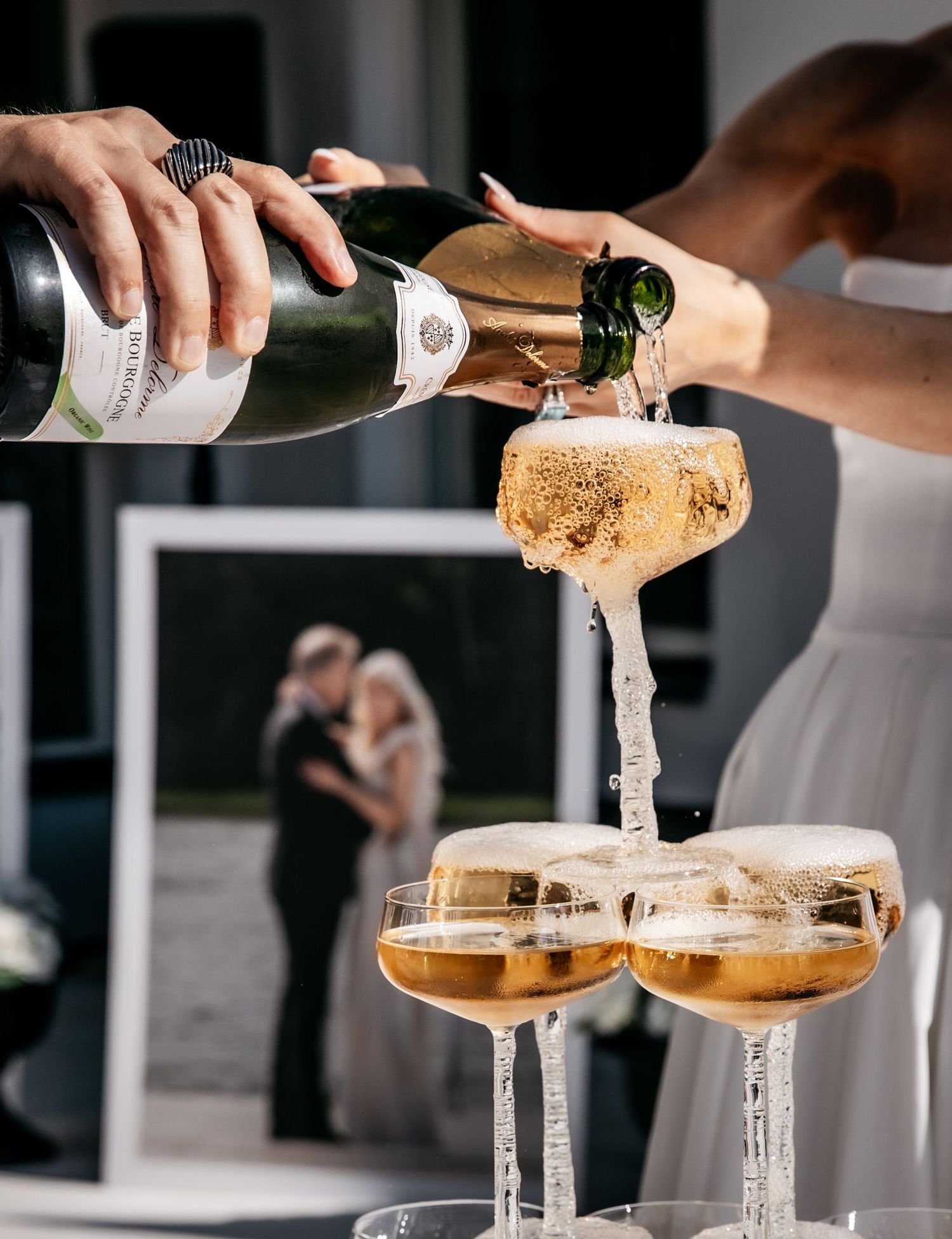 Champagne tower being poured at a wedding reception with bride and groom photo in background.