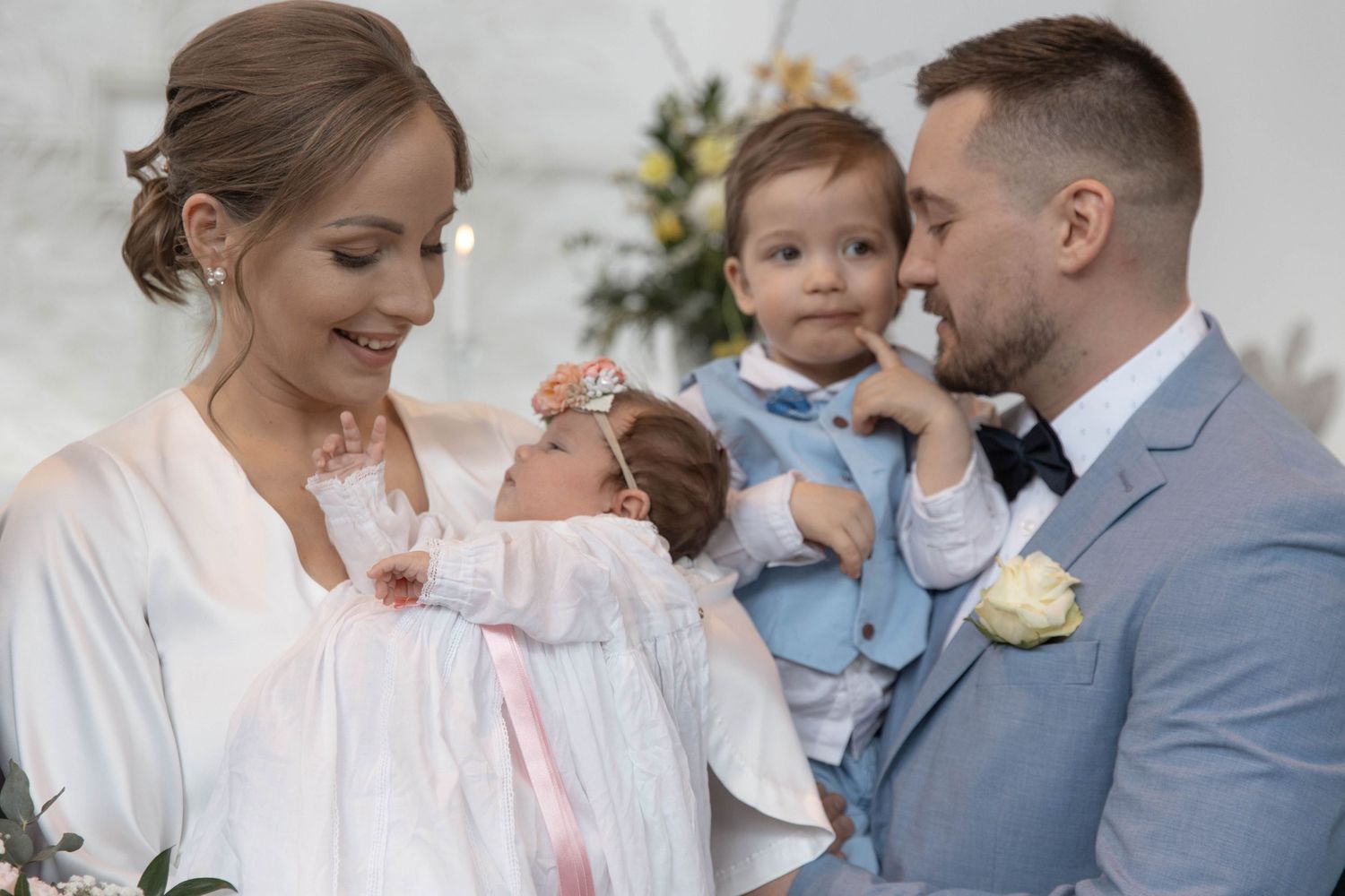 Happy family at christening ceremony with mother holding baby girl and father holding toddler son.