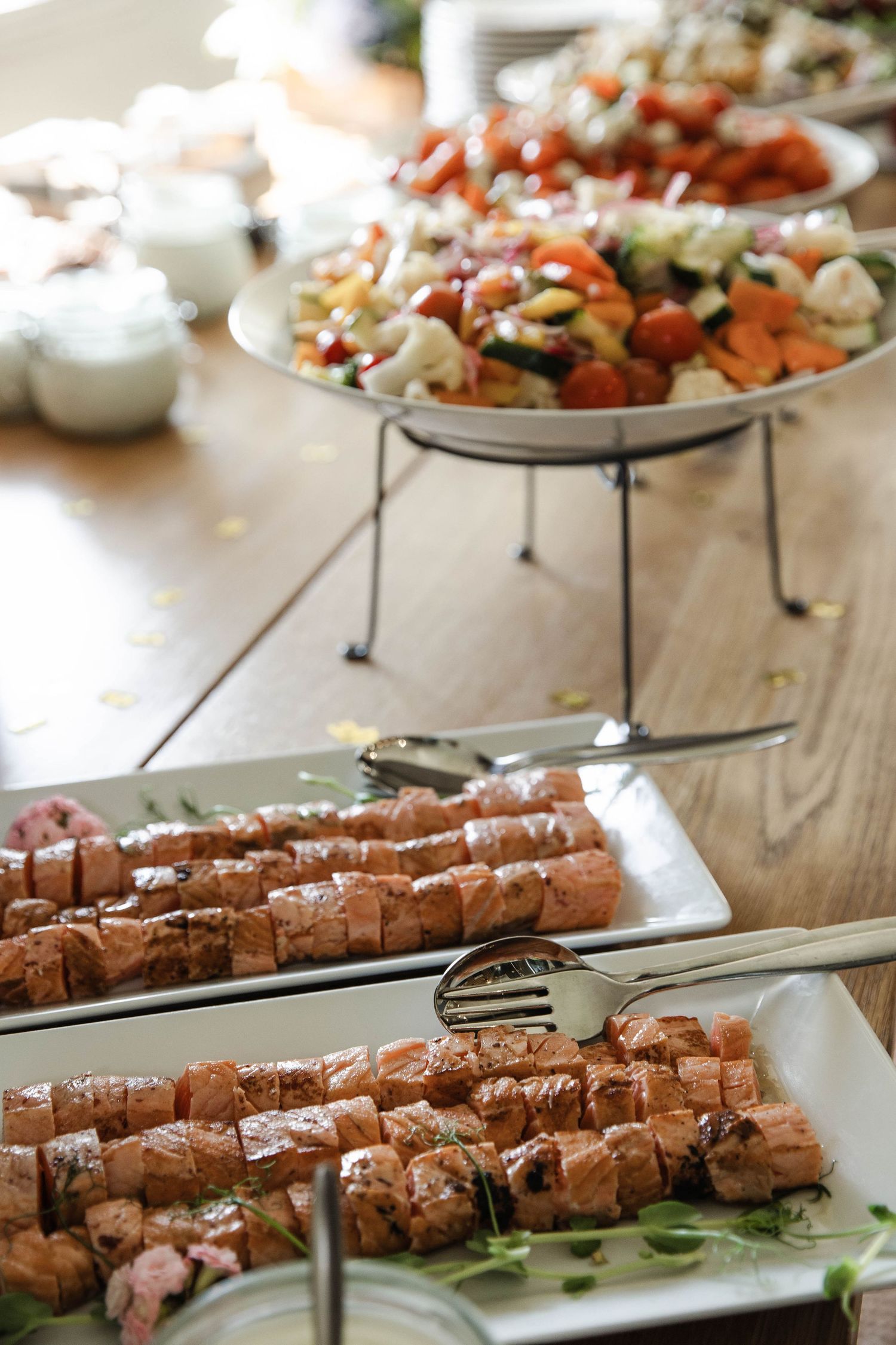 Elegant catered buffet spread featuring grilled salmon skewers and fresh vegetable salad platters.