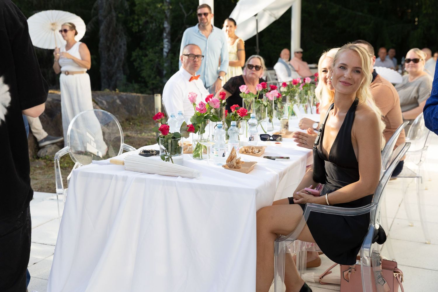 Guests enjoy an elegant outdoor wedding reception dinner with floral centerpieces and clear ghost chairs.