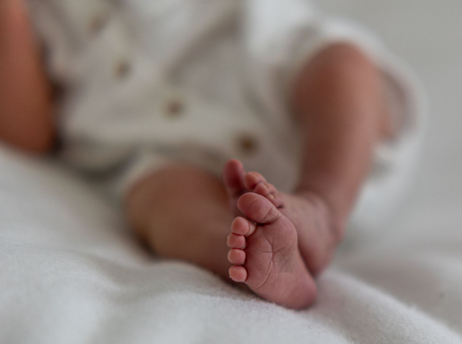 Close-up of newborn baby tiny feet and toes resting on soft white blanket.