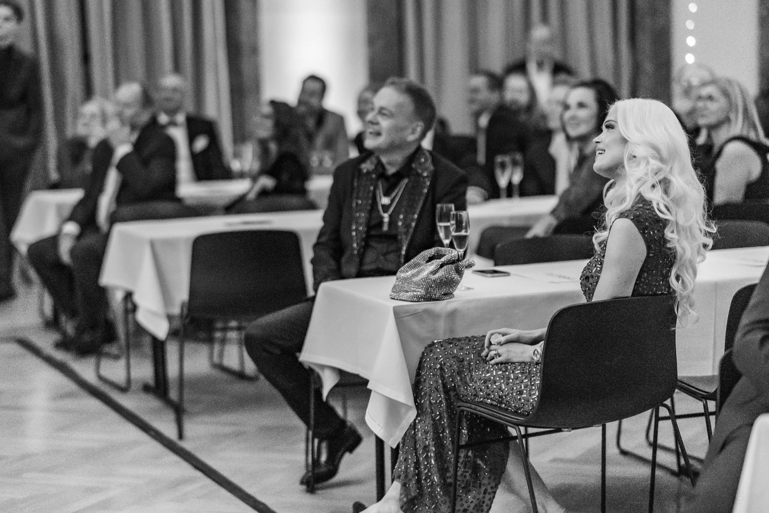 Black and white photo of elegantly dressed guests smiling and socializing at a formal event dinner.
