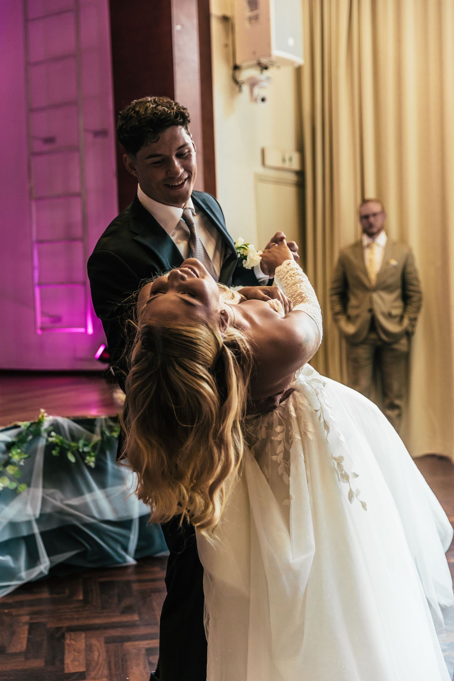 Groom dipping bride during first dance at wedding reception with guest watching in background.
