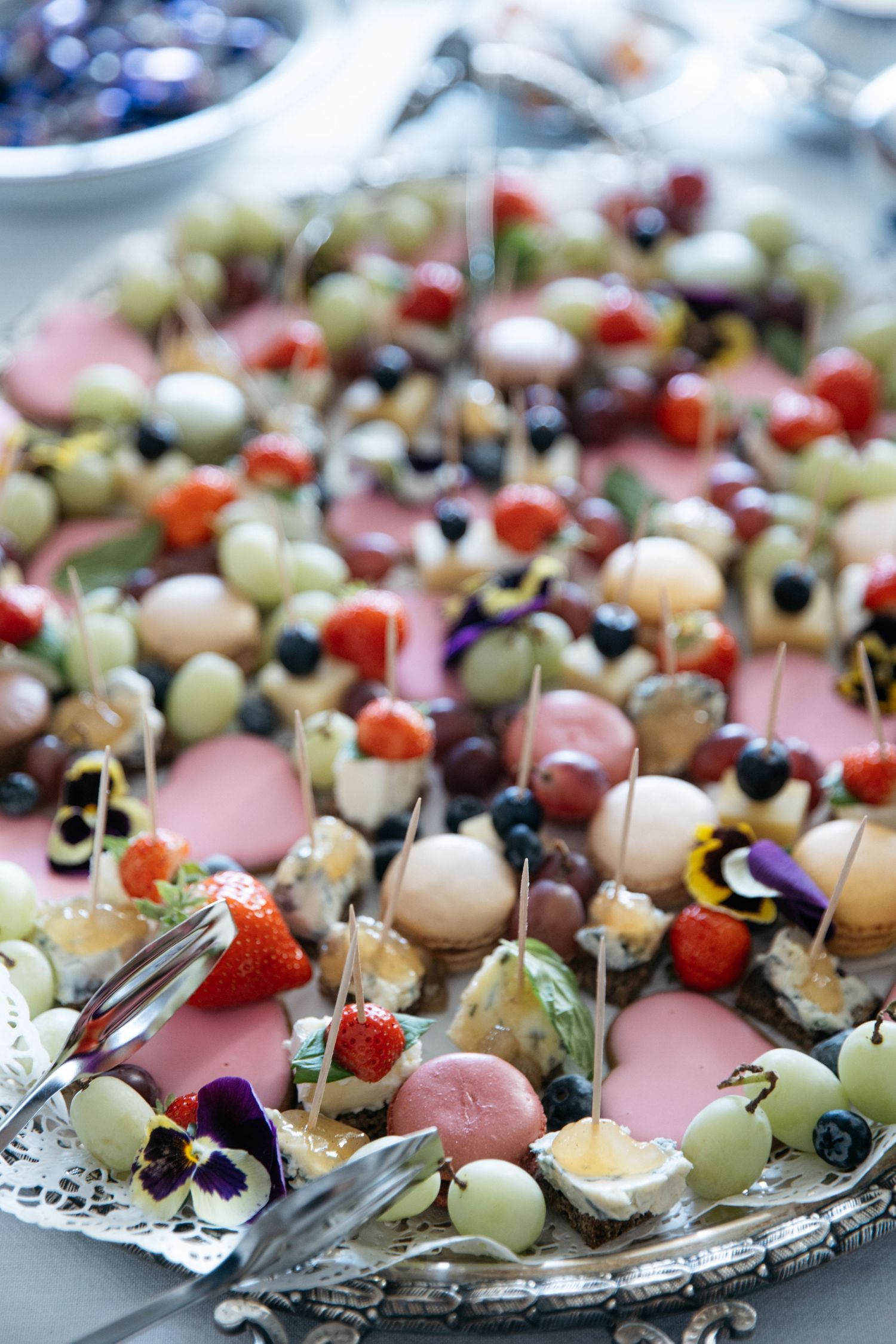 Elegant silver platter of fruit skewers with strawberries, grapes, melon and edible flowers at a party.