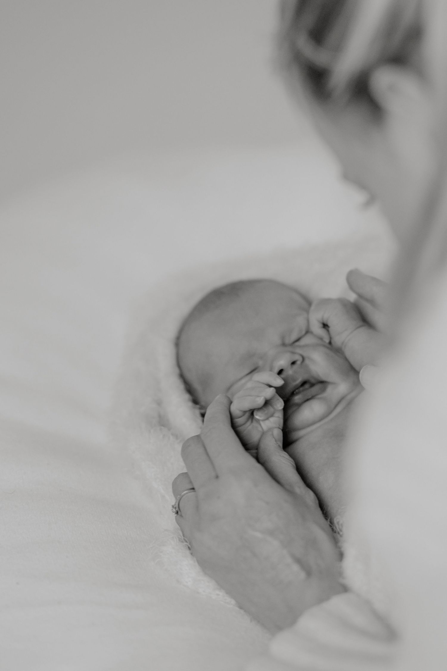 Black and white photo of a newborn baby sleeping while mother gently touches its face with ringed hand.
