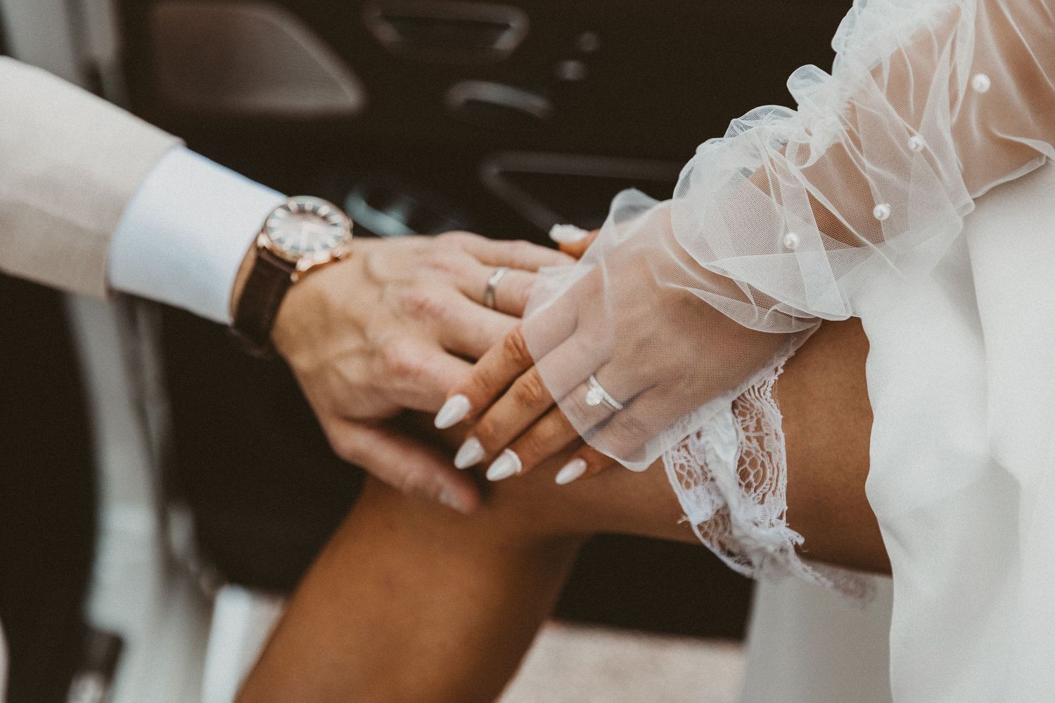 Close-up of bride and groom holding hands showing wedding rings, bride wearing lace sleeve wedding dress.
