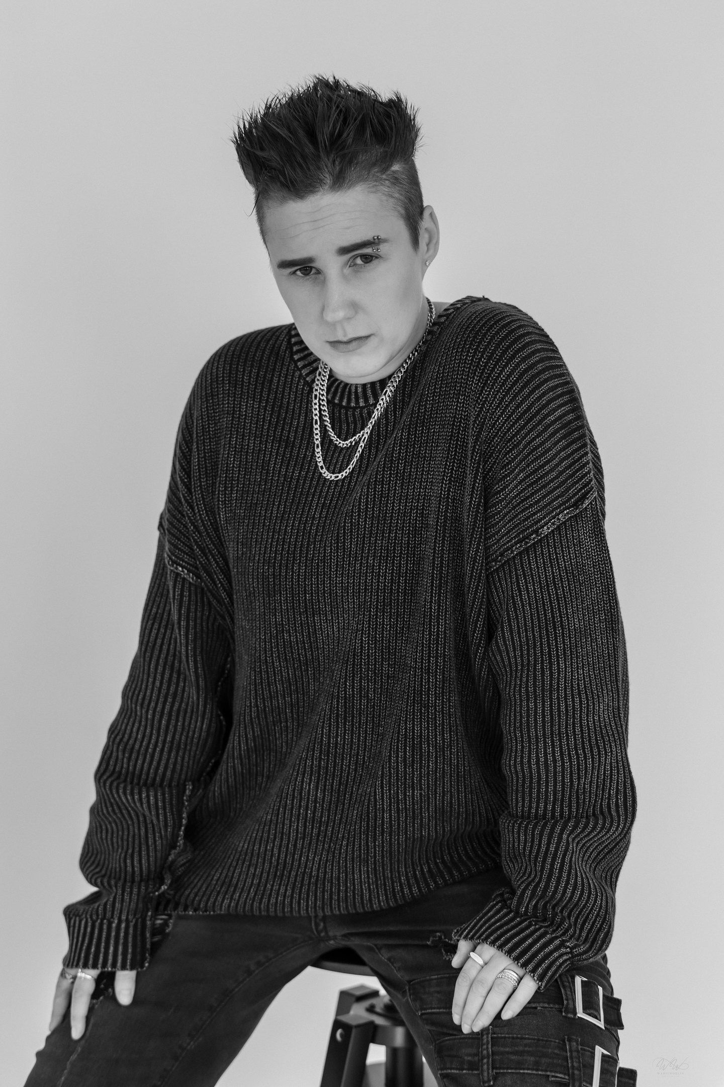 Young man in oversized knit sweater with chain necklace poses in black and white portrait.