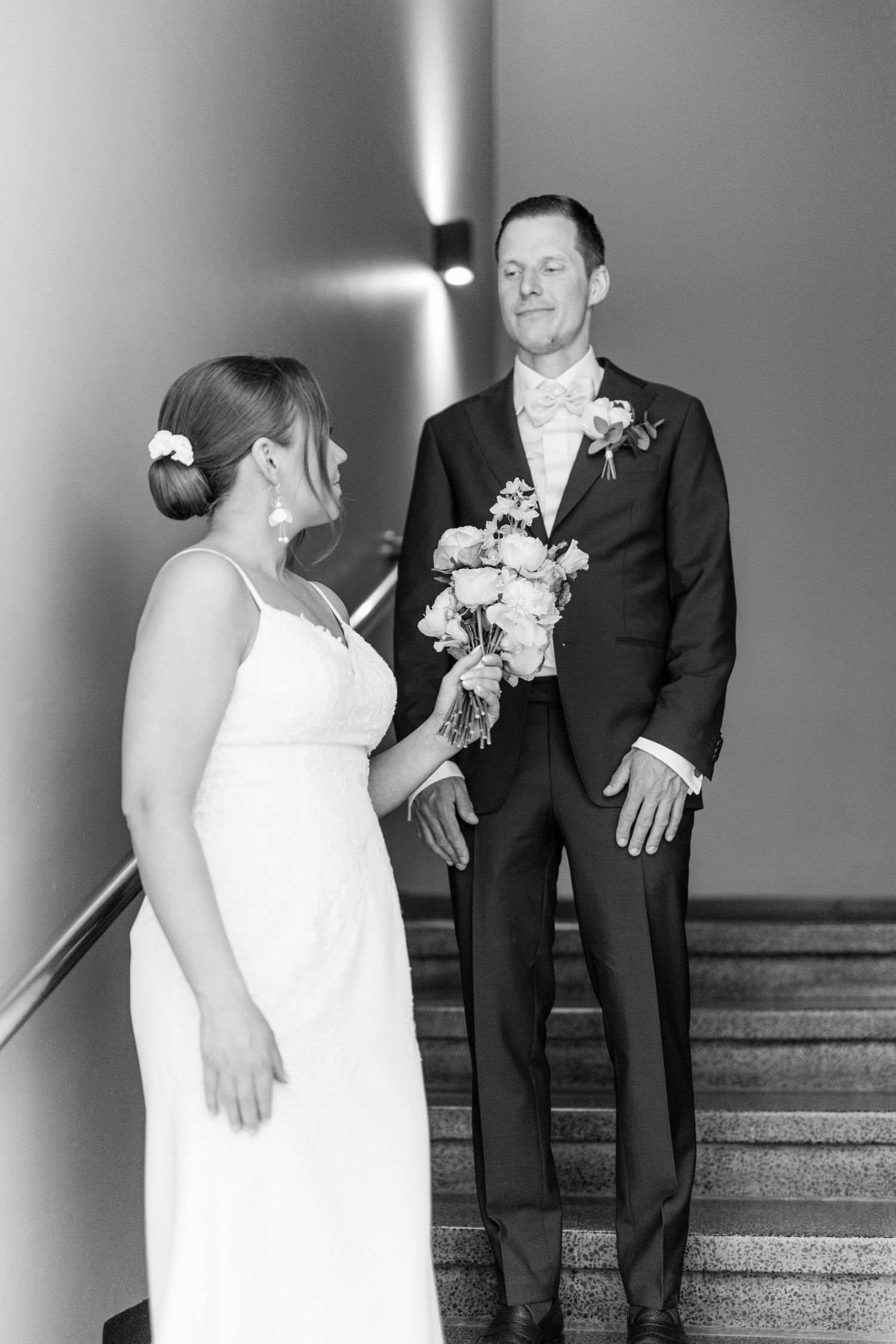Black and white photo of bride and groom on staircase, groom holding bridal bouquet of roses.