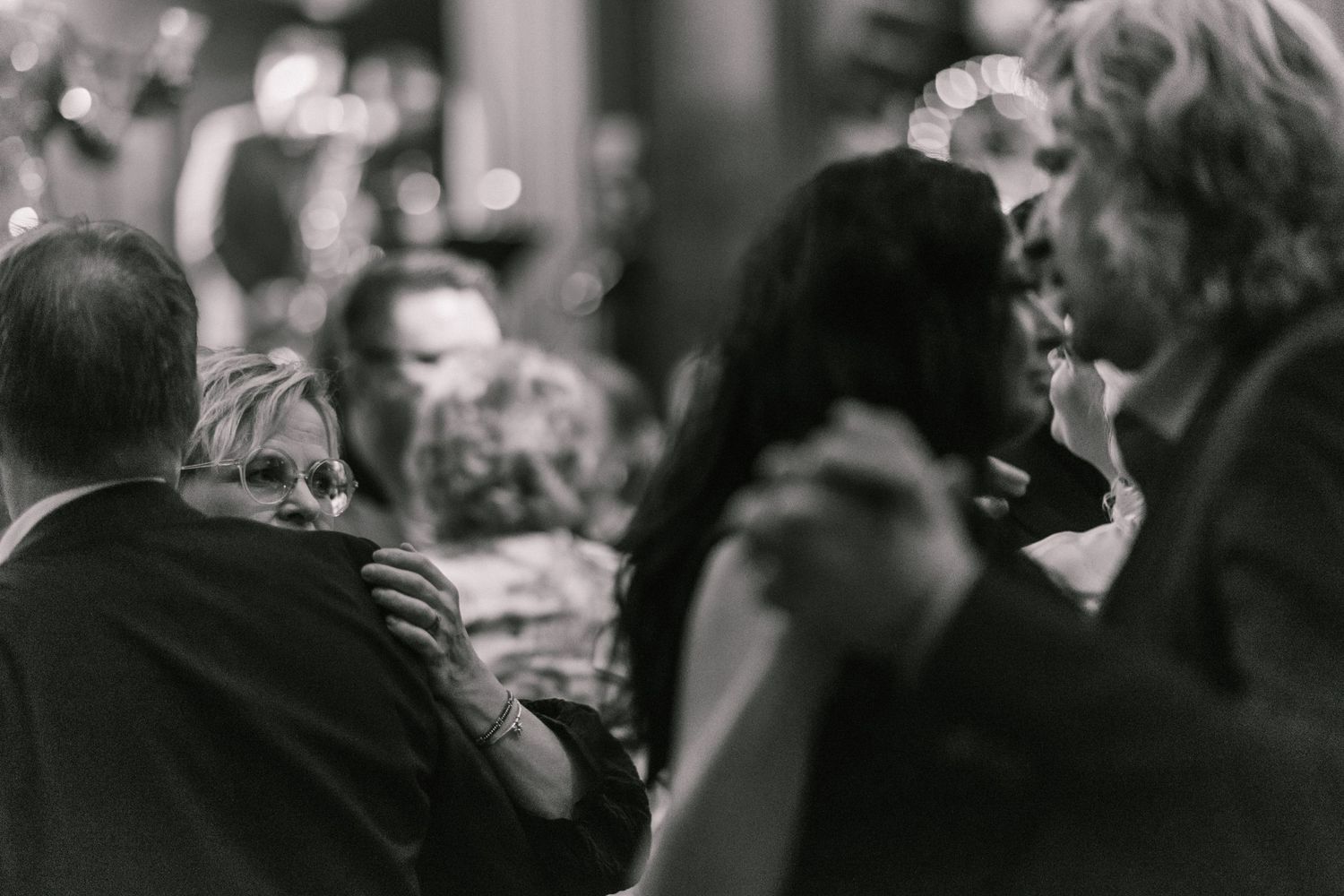 Black and white candid photo of guests embracing and dancing at an intimate evening celebration.
