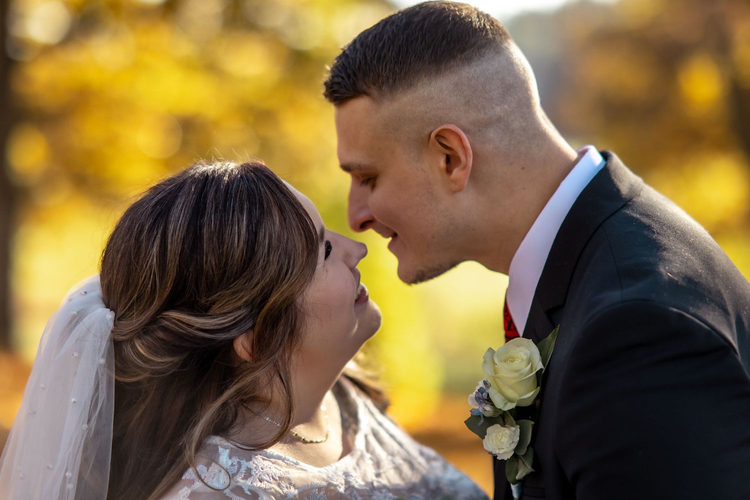 Bride and groom leaning in for a kiss surrounded by golden autumn foliage outdoors.