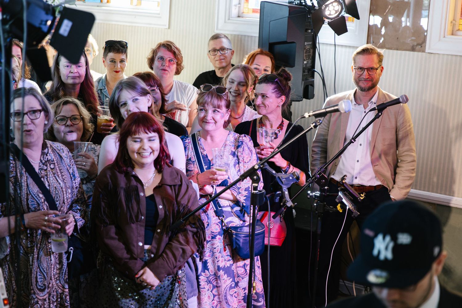 A lively group of people gathered around microphones at an indoor event with stage lighting.