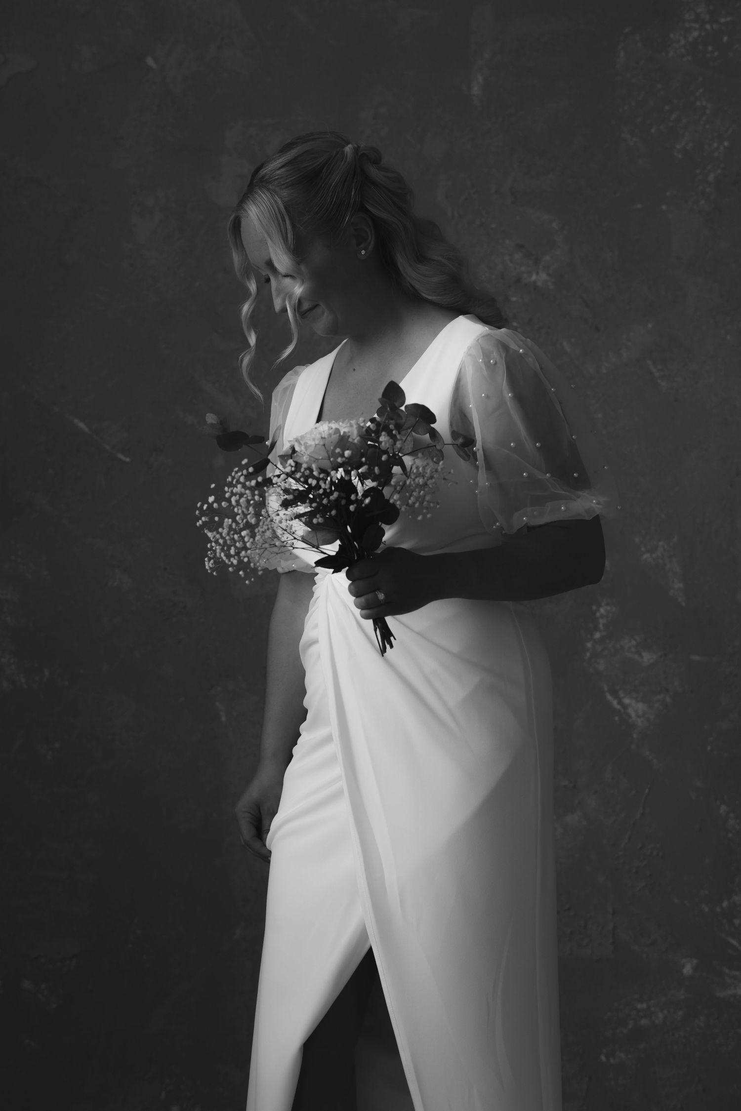 Elegant bride in white gown holding floral bouquet, black and white studio portrait photography.
