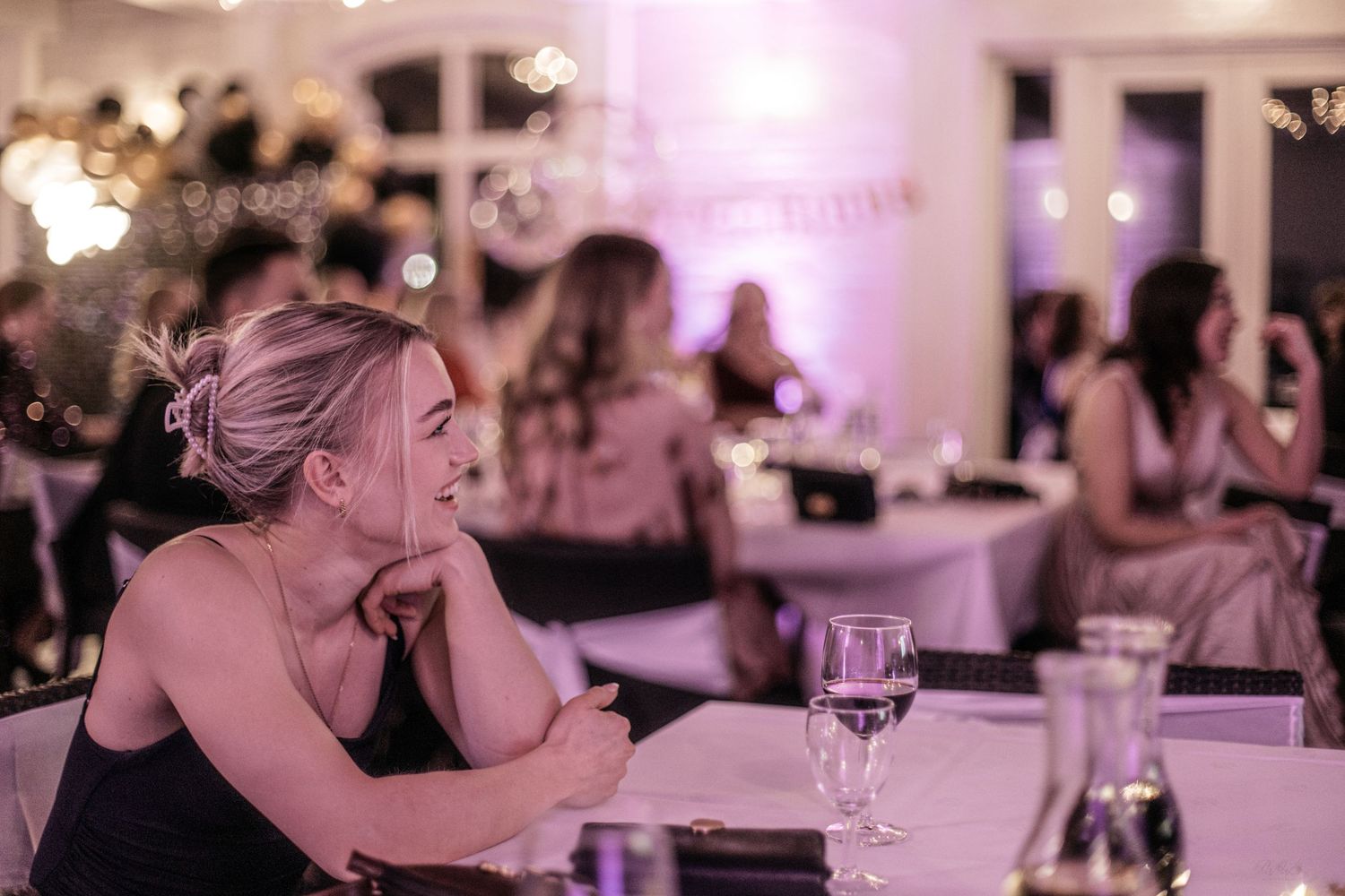 Blonde woman in black dress sitting pensively at a table during an elegant evening gala.
