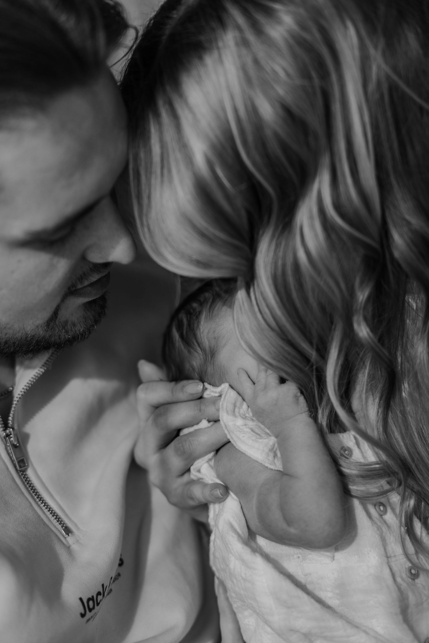 Black and white photo of parents lovingly holding their newborn baby together in an intimate family portrait.