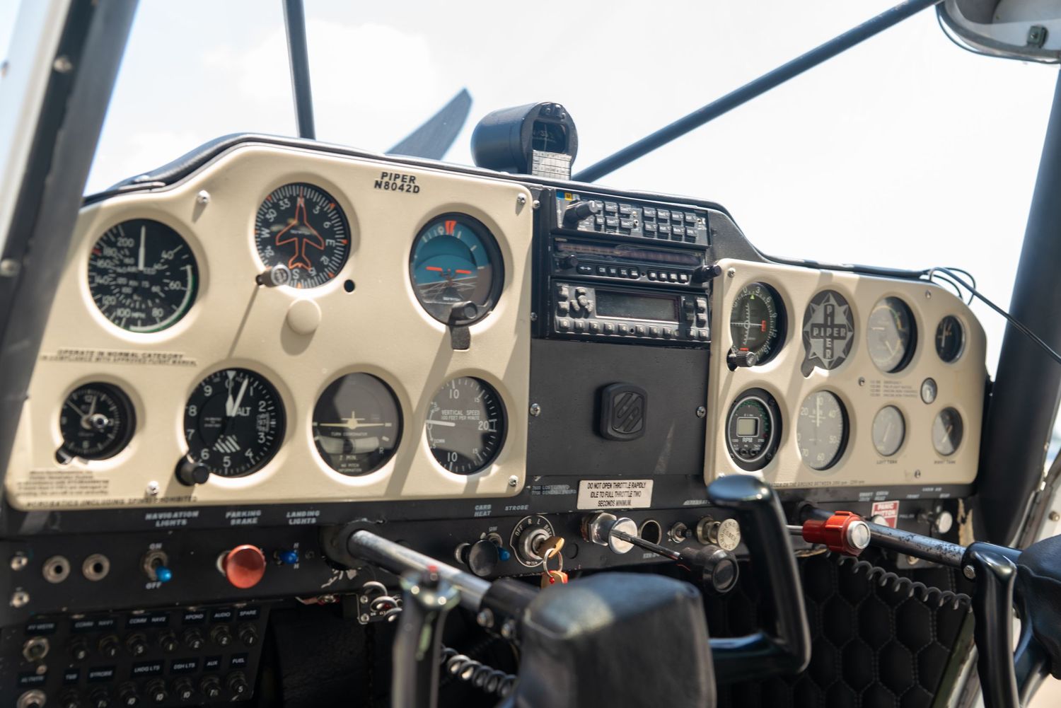 Vintage small aircraft cockpit dashboard with analog flight instruments, gauges, and controls on a beige panel.