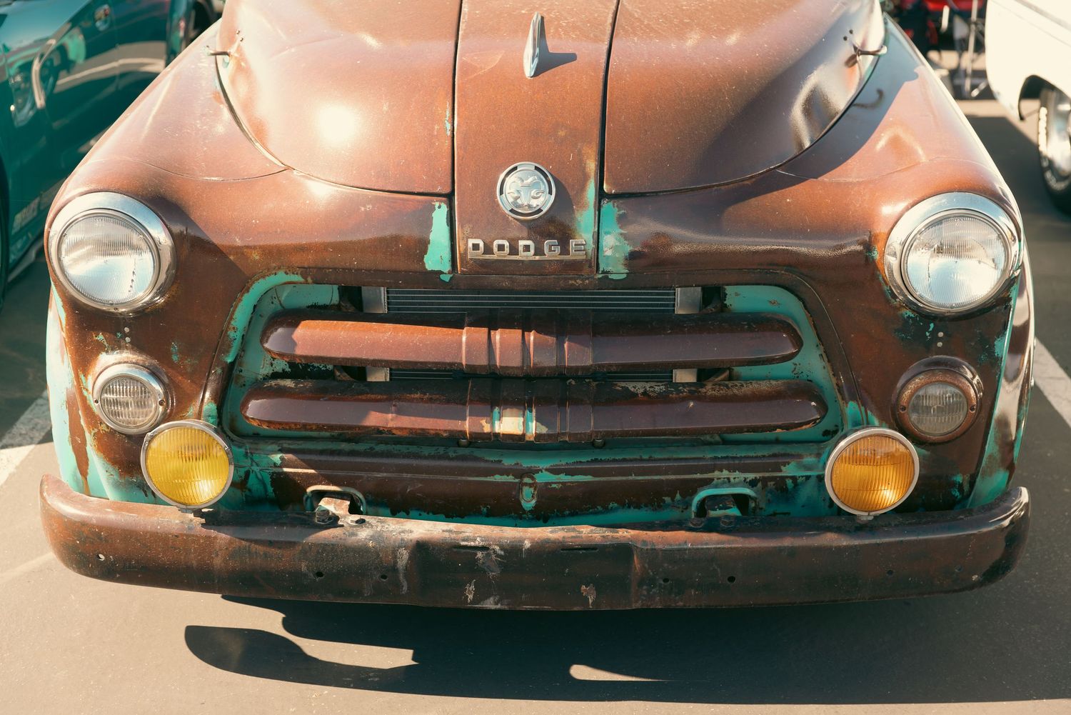Rusty vintage Dodge truck front view showing aged patina, classic grille, and round headlights in an outdoor setting.