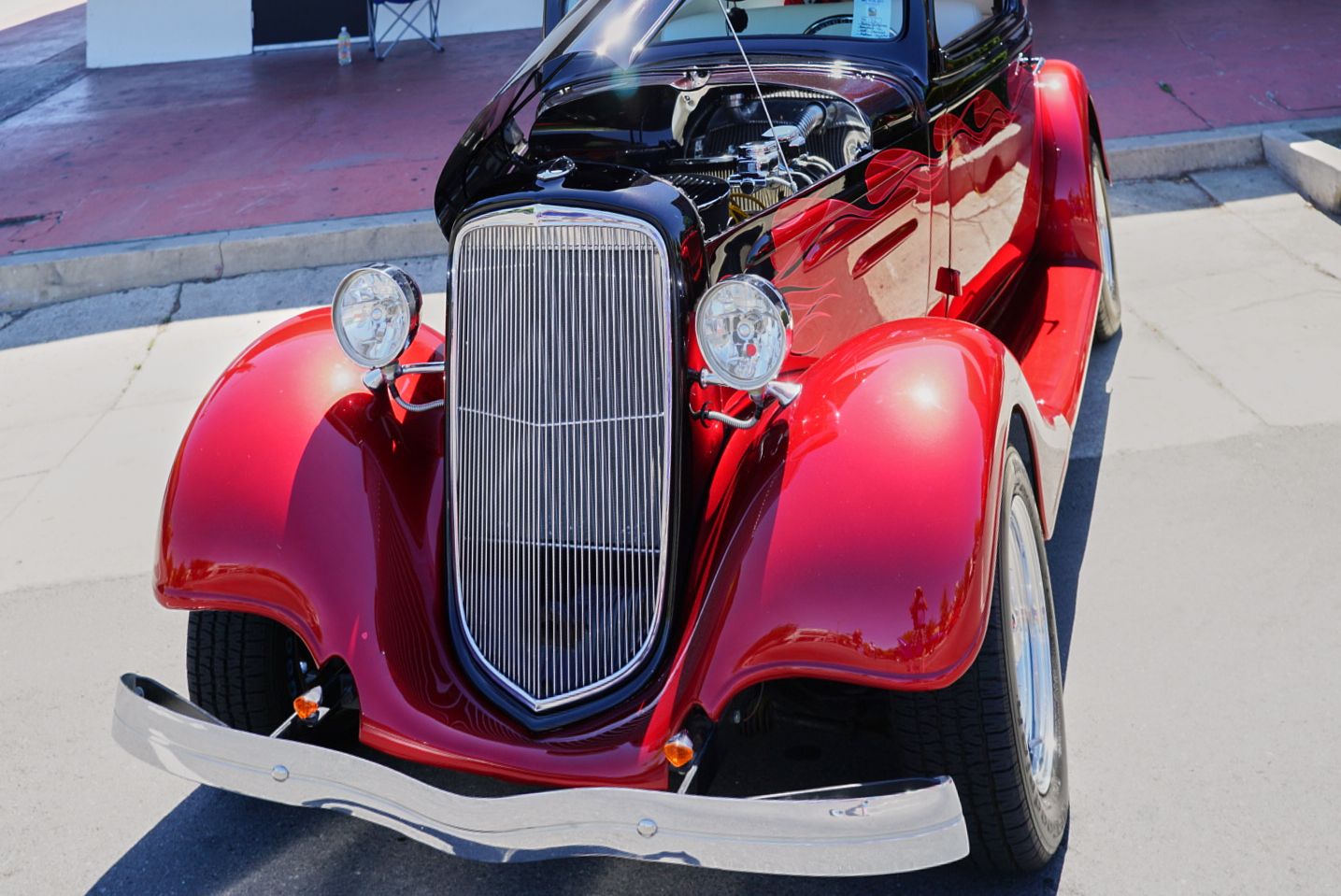 A shiny red 1930s vintage convertible classic car with chrome grille parked outdoors in sunlight.