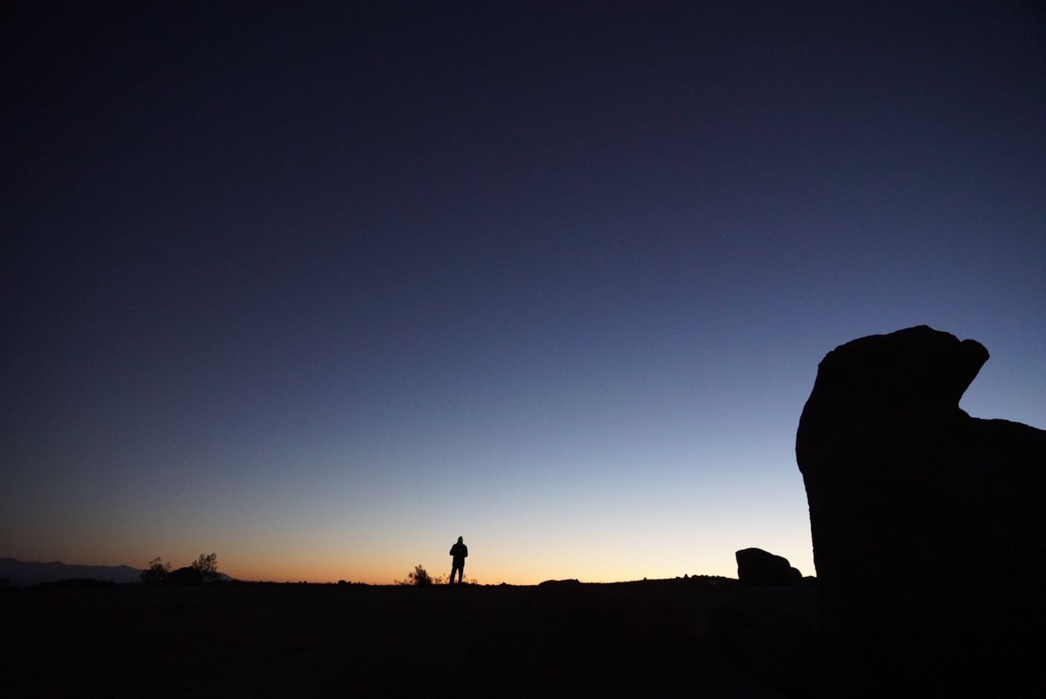 Person standing in desert silhouetted against colorful orange and blue sunset.