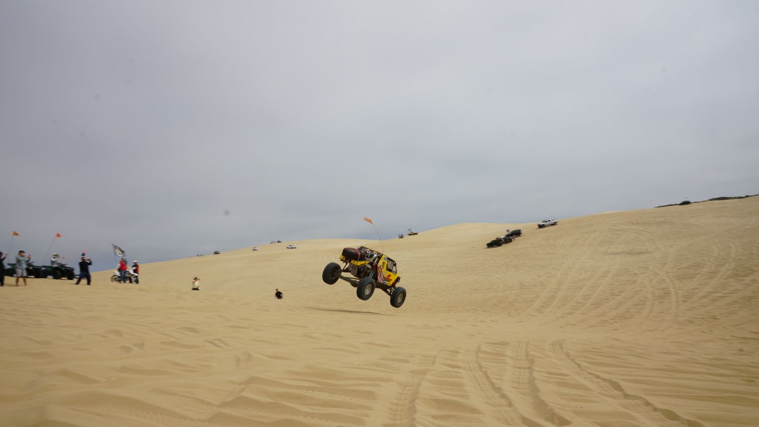 Yellow dune buggy catches air while jumping over sandy desert dunes at an off-road racing event.